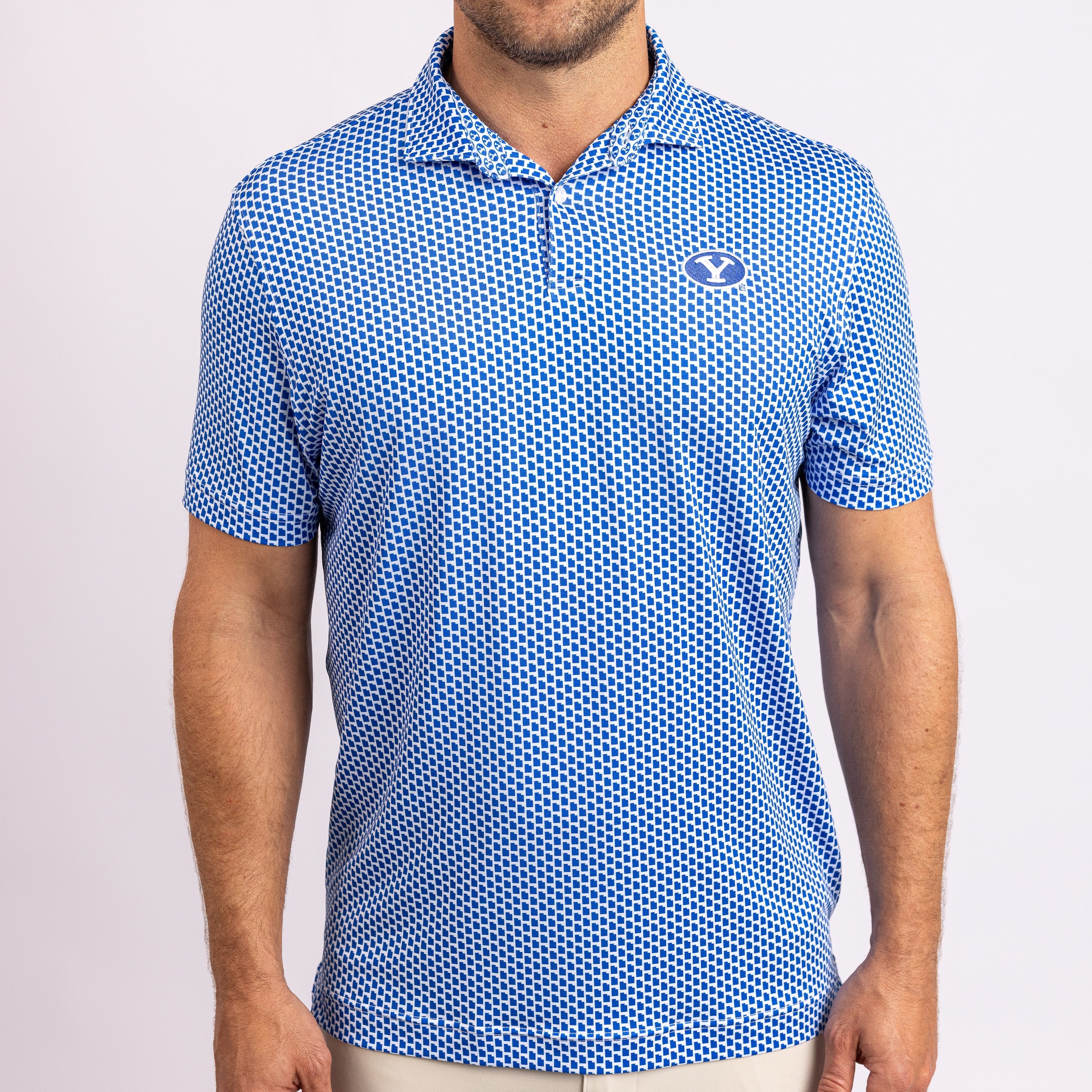 A man wearing a blue and white patterned short-sleeve polo shirt with a small embroidered logo on the left chest, photographed against a light gray studio background.