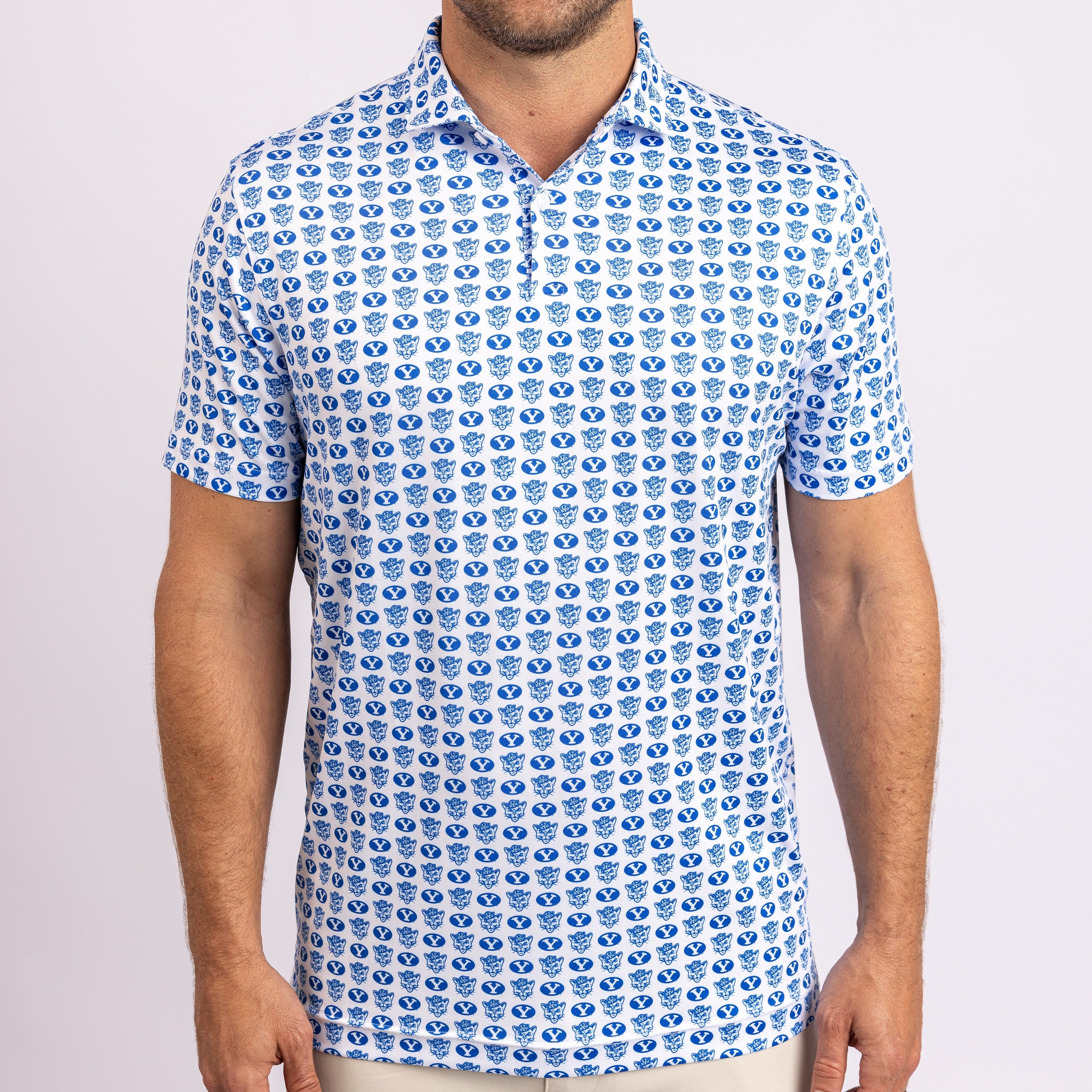 A man wearing a short-sleeve polo shirt with a repeating blue and white pattern of stylized shield emblems, shown from the neck down against a light gray studio background.