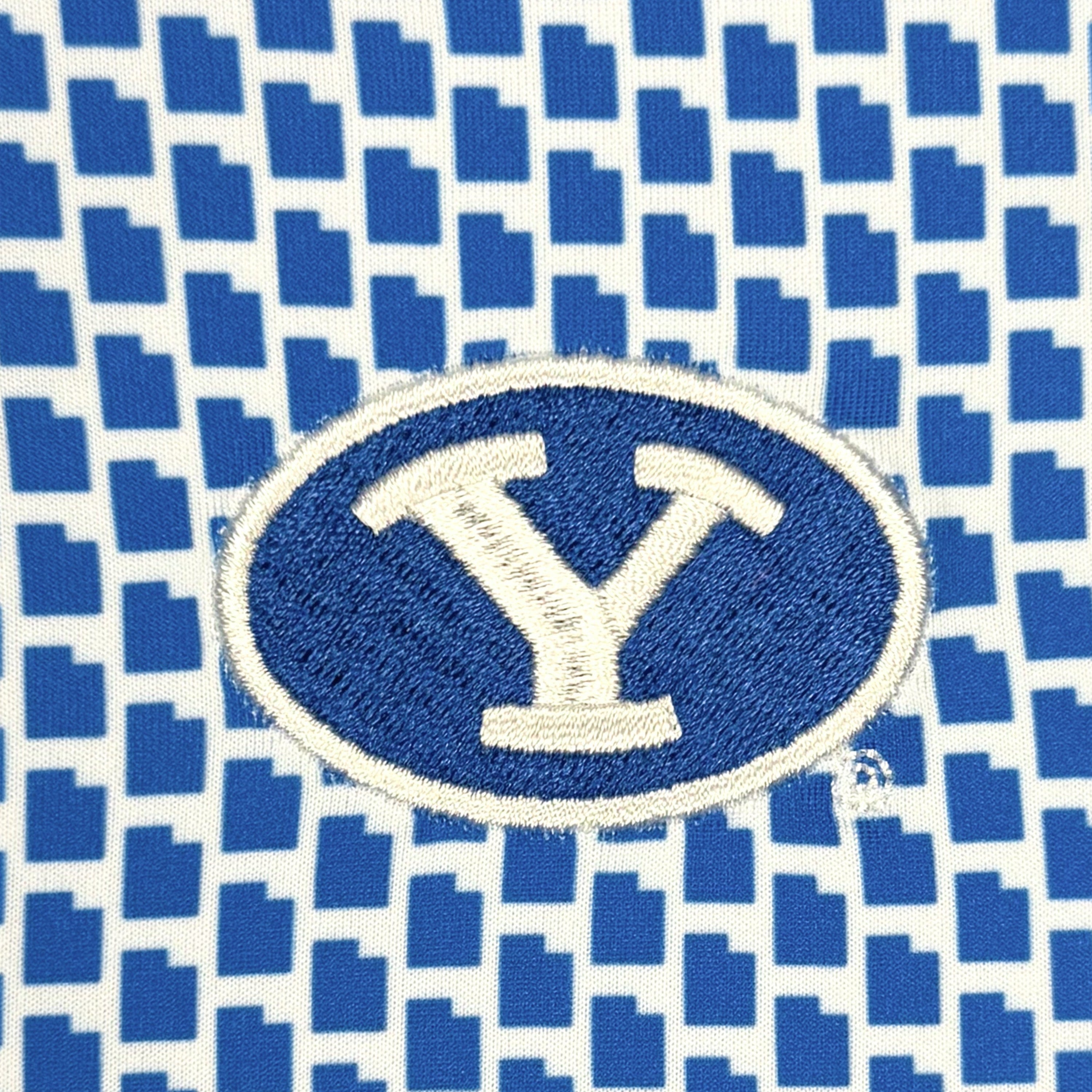 A close-up of a blue and white patterned fabric featuring an embroidered oval logo with a large white letter Y on a blue background.