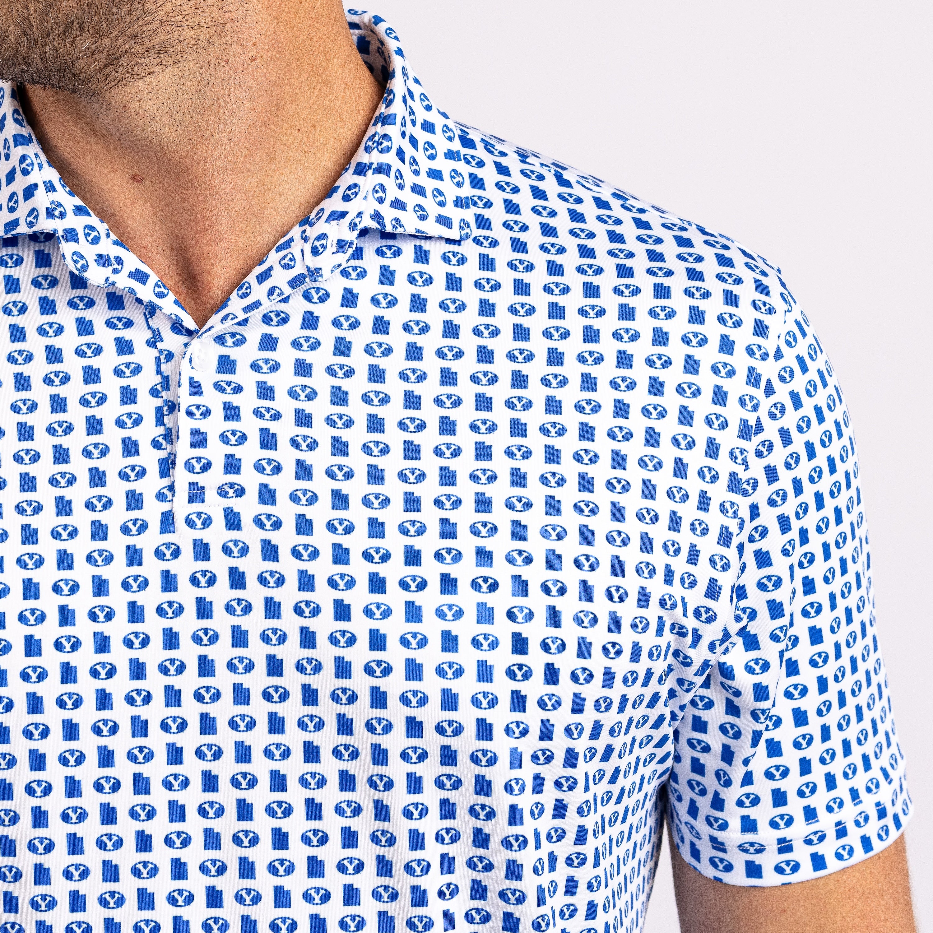 Close-up of a man wearing a short-sleeve polo shirt with a blue and white repeating monogram pattern, shown from the neck to the upper chest against a light gray background.