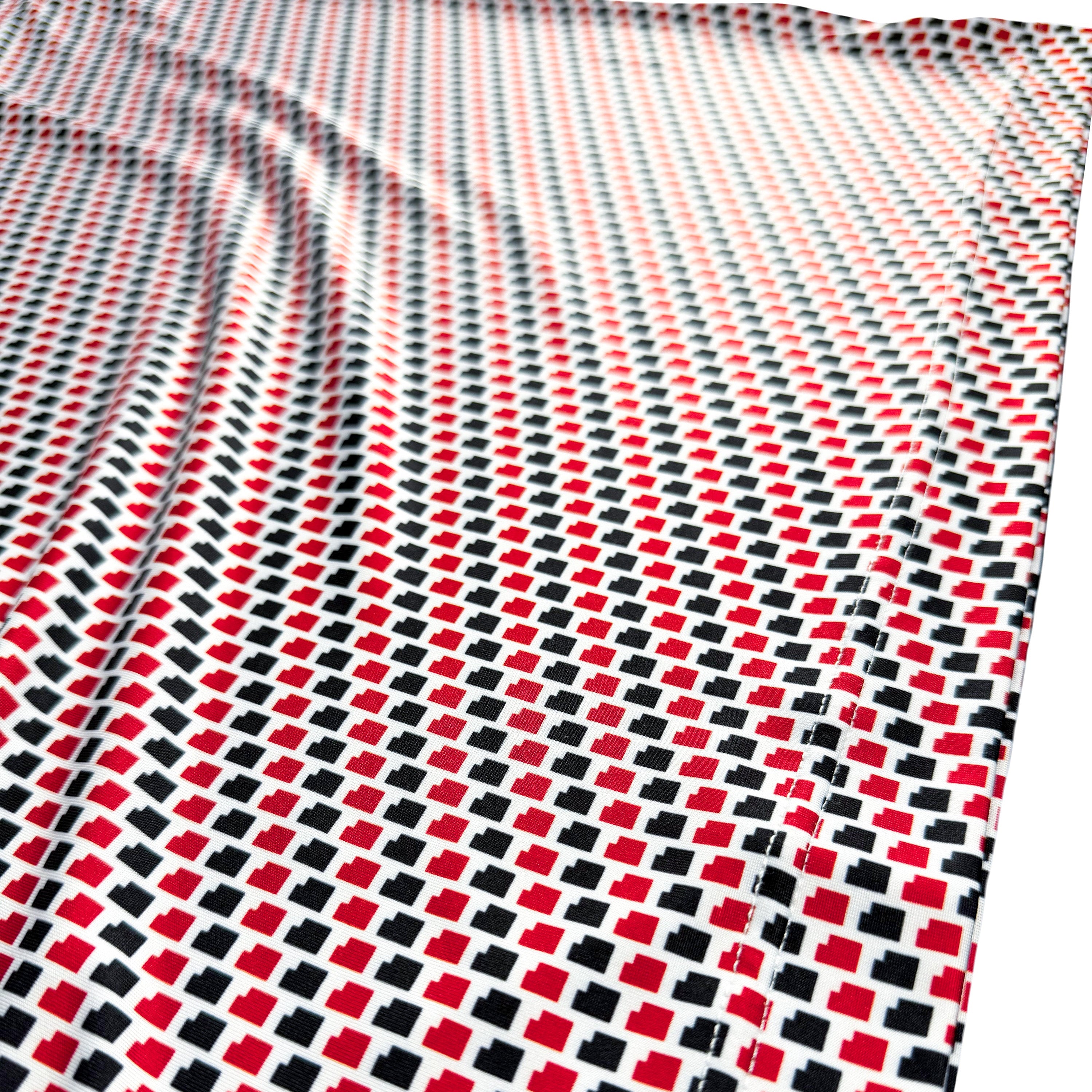 A close-up of a patterned fabric with a repeating geometric design of red, black, and white squares on a white background.