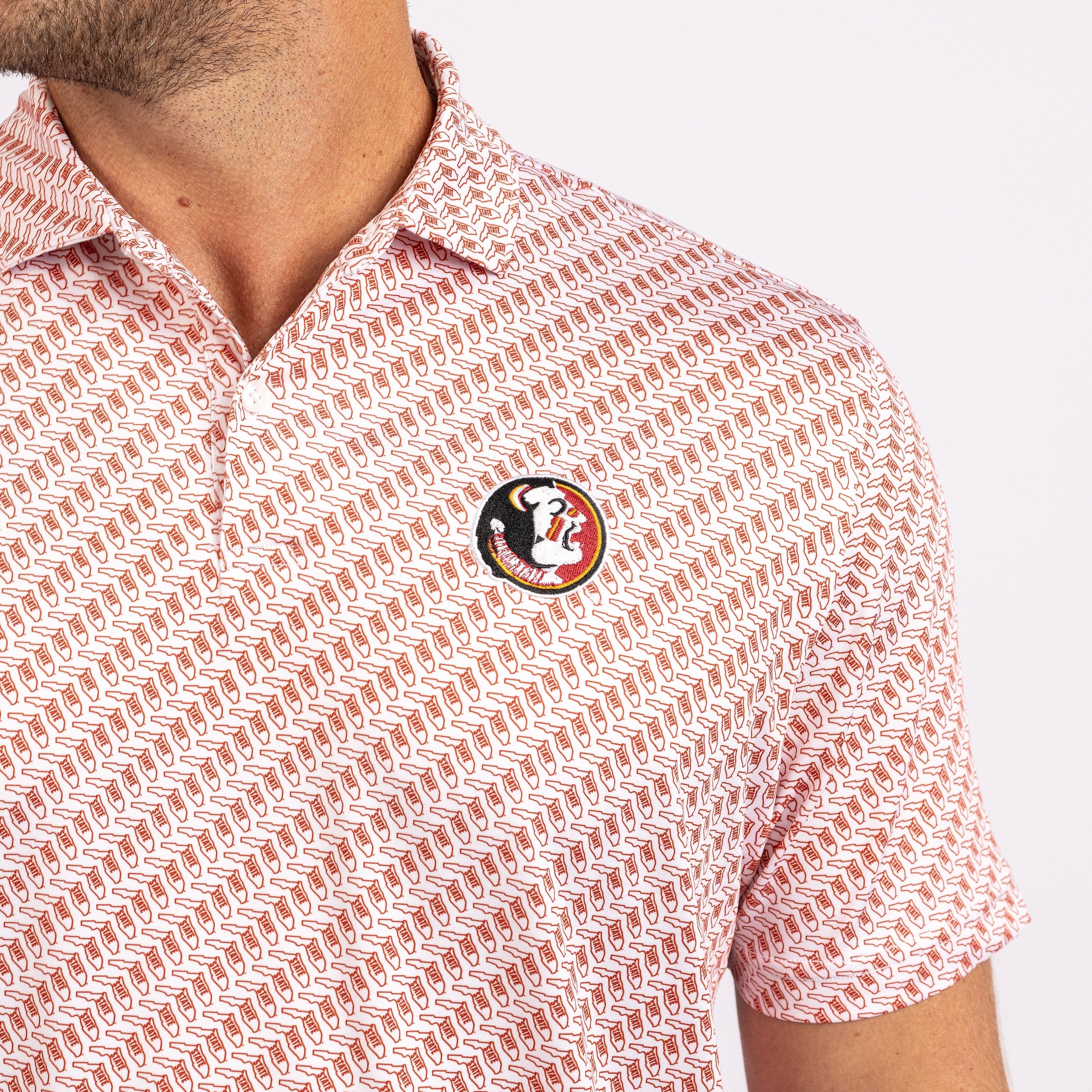 Close-up of a man wearing a short-sleeve polo shirt with a repeating geometric pattern in white and terracotta red, featuring a Florida State Seminoles logo patch on the chest.