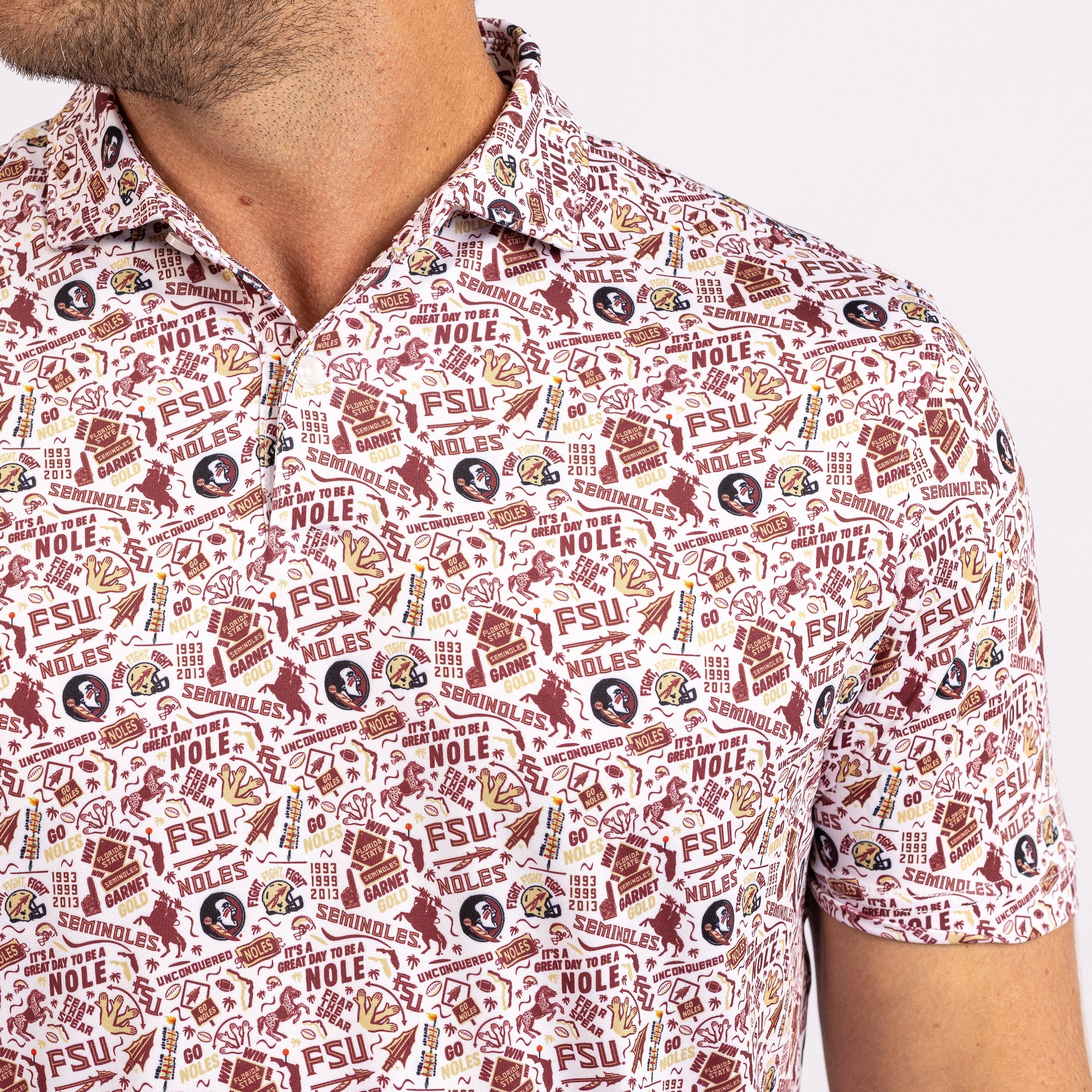 A close-up of a man wearing a short-sleeve collared button-up shirt with an all-over Florida State University graphic print in maroon, gold, and white.