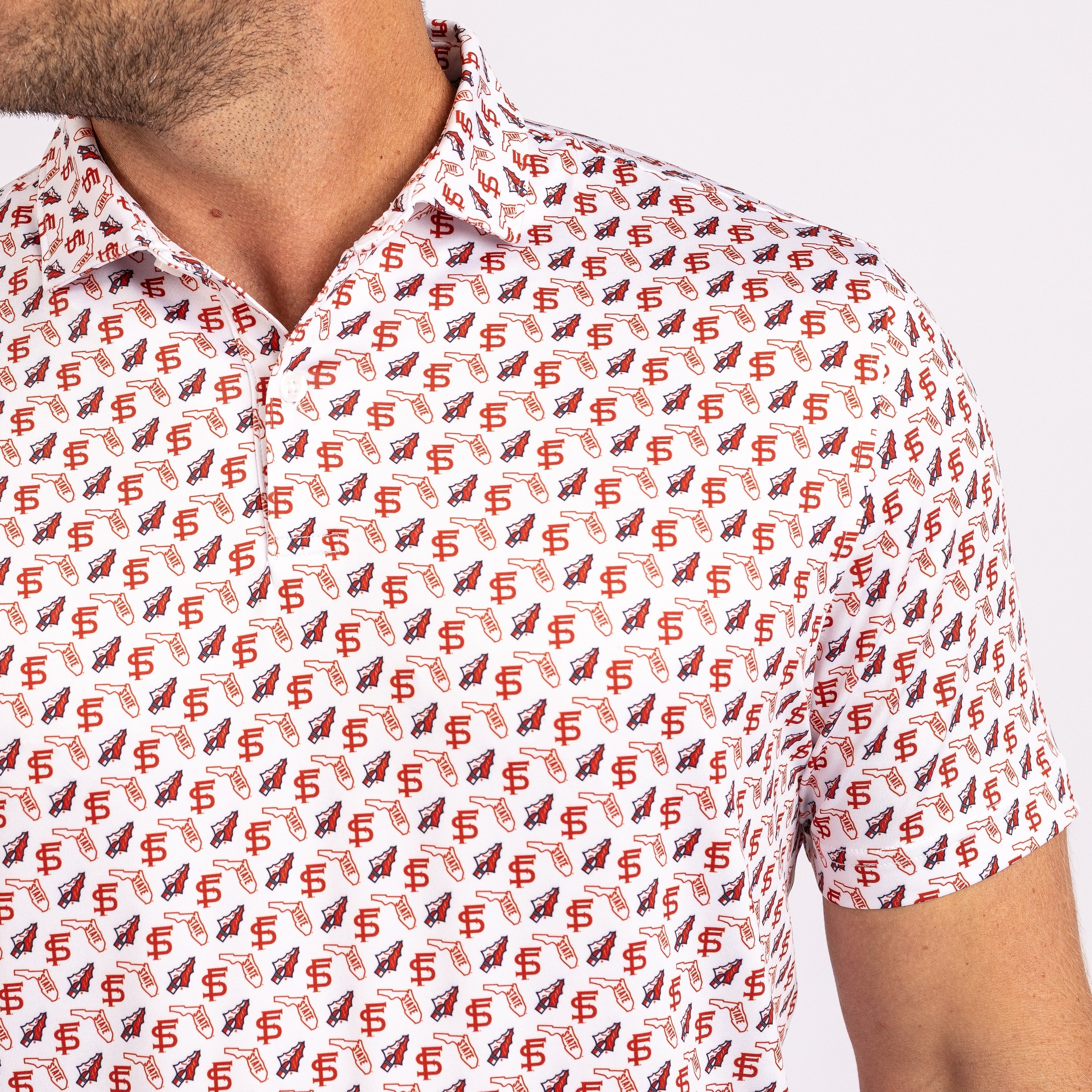 A close-up of a man wearing a short-sleeve collared button-up shirt with an all-over repeating pattern of red and navy football helmets and dollar signs on a white background.