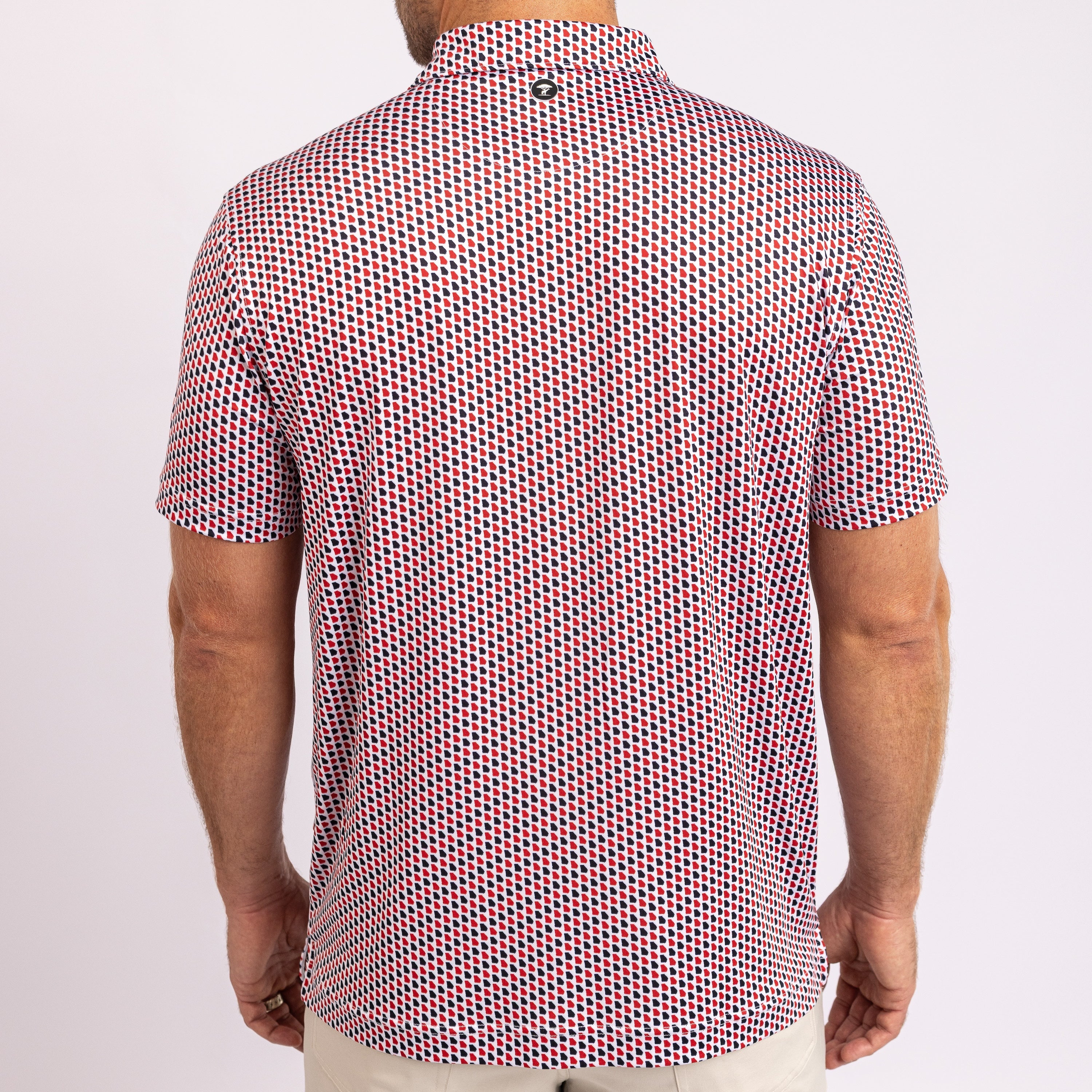 A man wearing a short-sleeve button-up shirt with a dense red, blue, and white geometric pattern, shown from the back against a plain white background.
