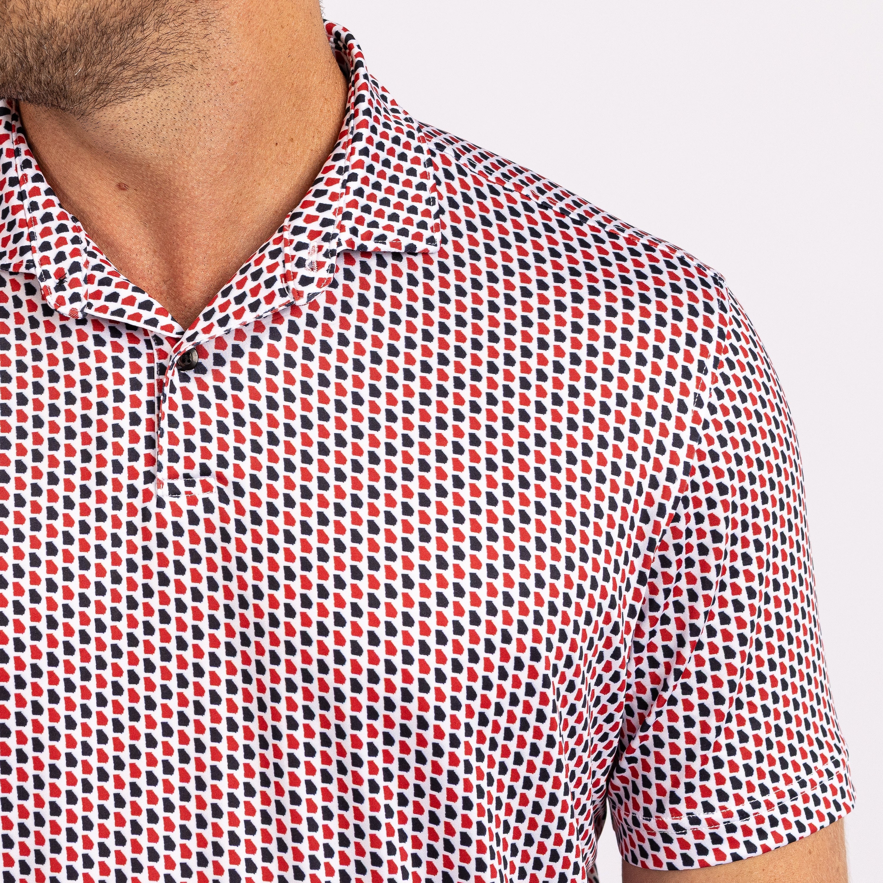 A man wearing a short-sleeve button-up shirt with a dense red, blue, and white geometric pattern