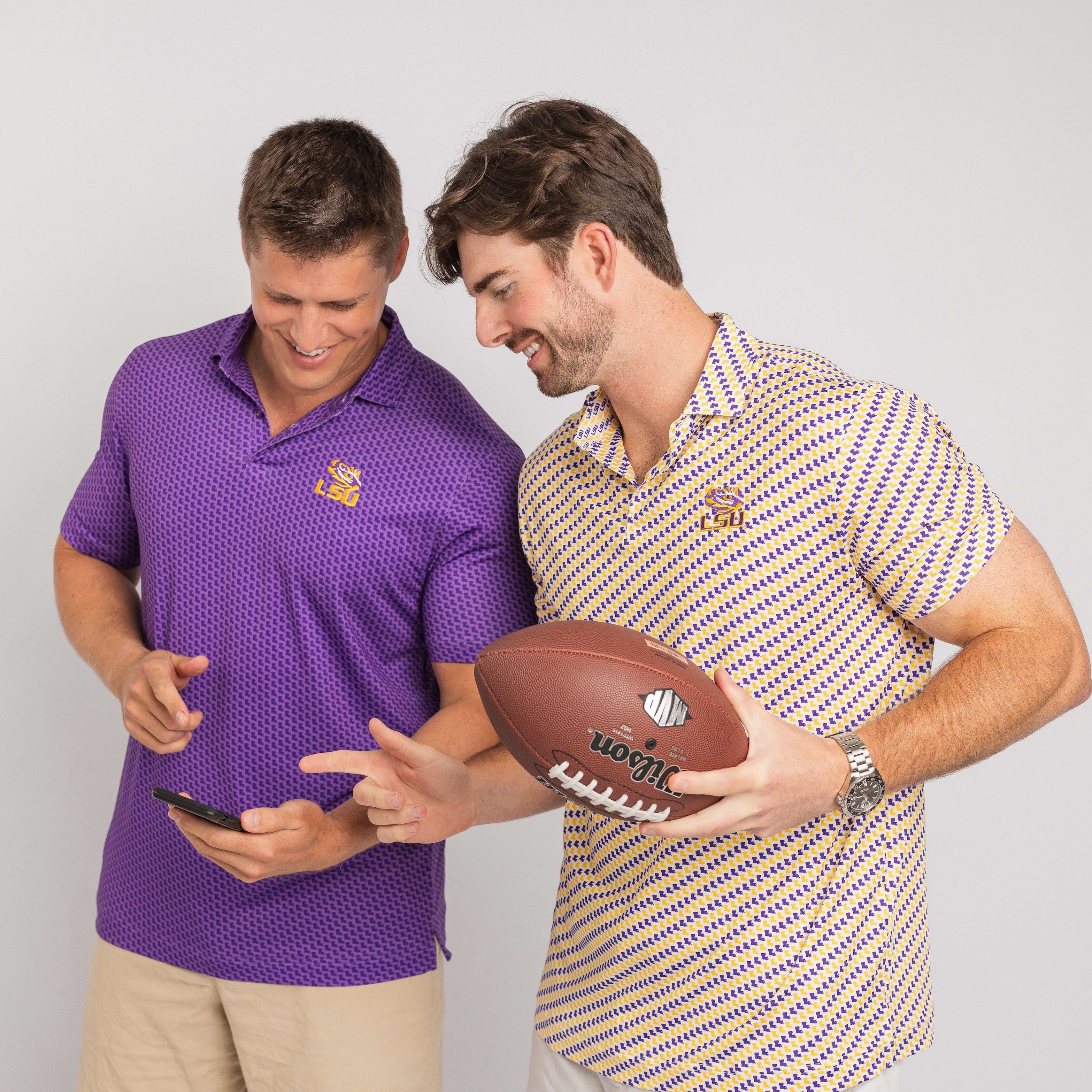 Two men, one in a purple shirt with a logo and the other in a patterned shirt holding a football, against a plain background.