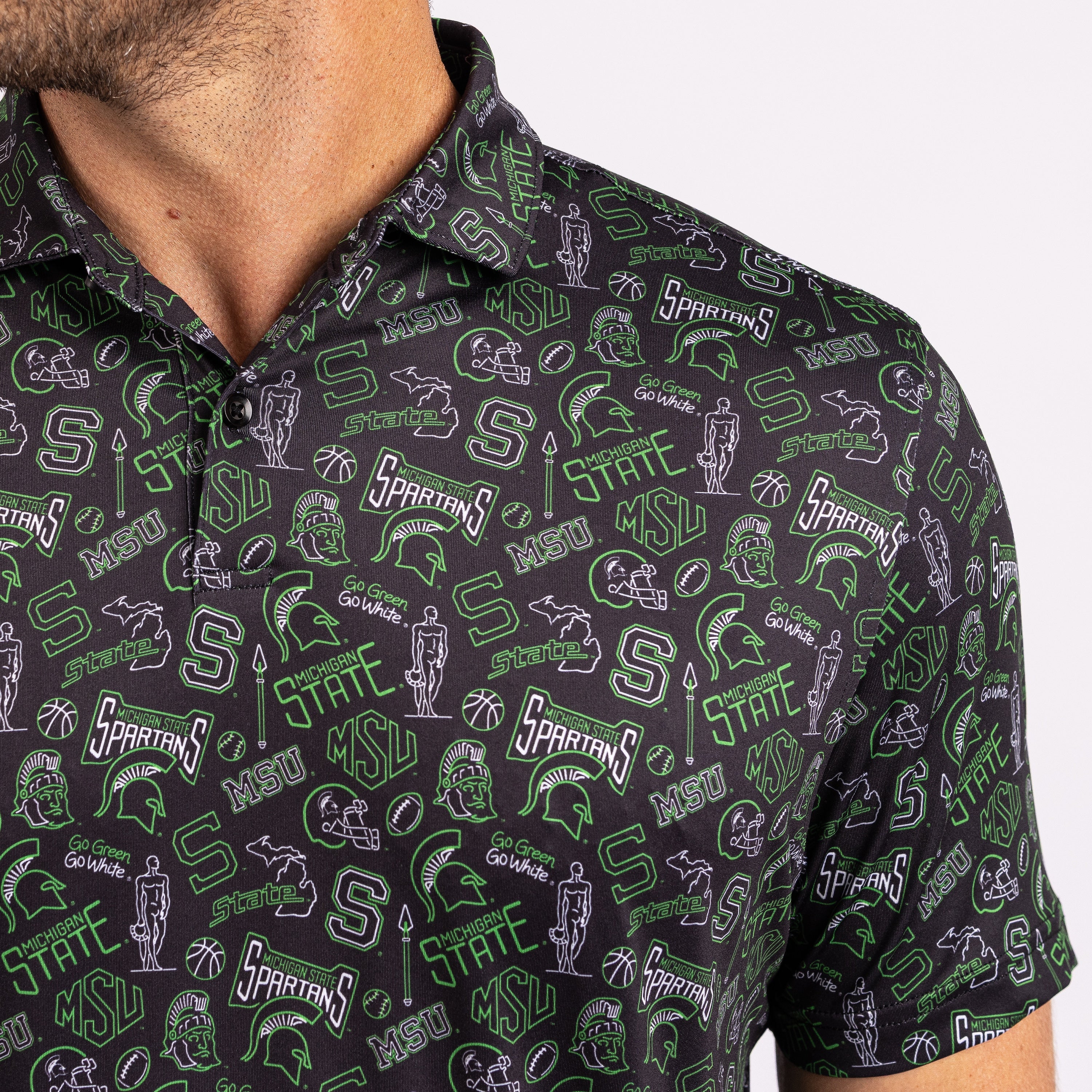 Close-up of a man wearing a short-sleeve polo shirt with an all-over Michigan State Spartans graphic print on a black background.