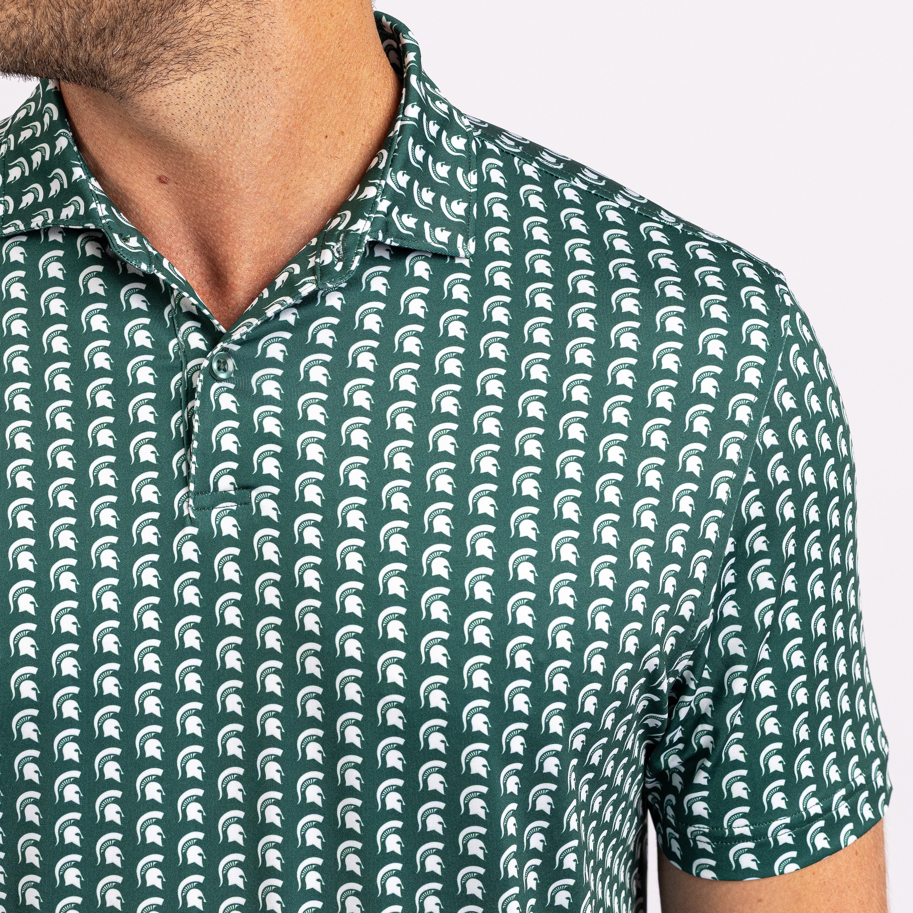 Close-up of a man wearing a short-sleeve polo shirt with a repeating white helmet logo pattern on a dark green background.