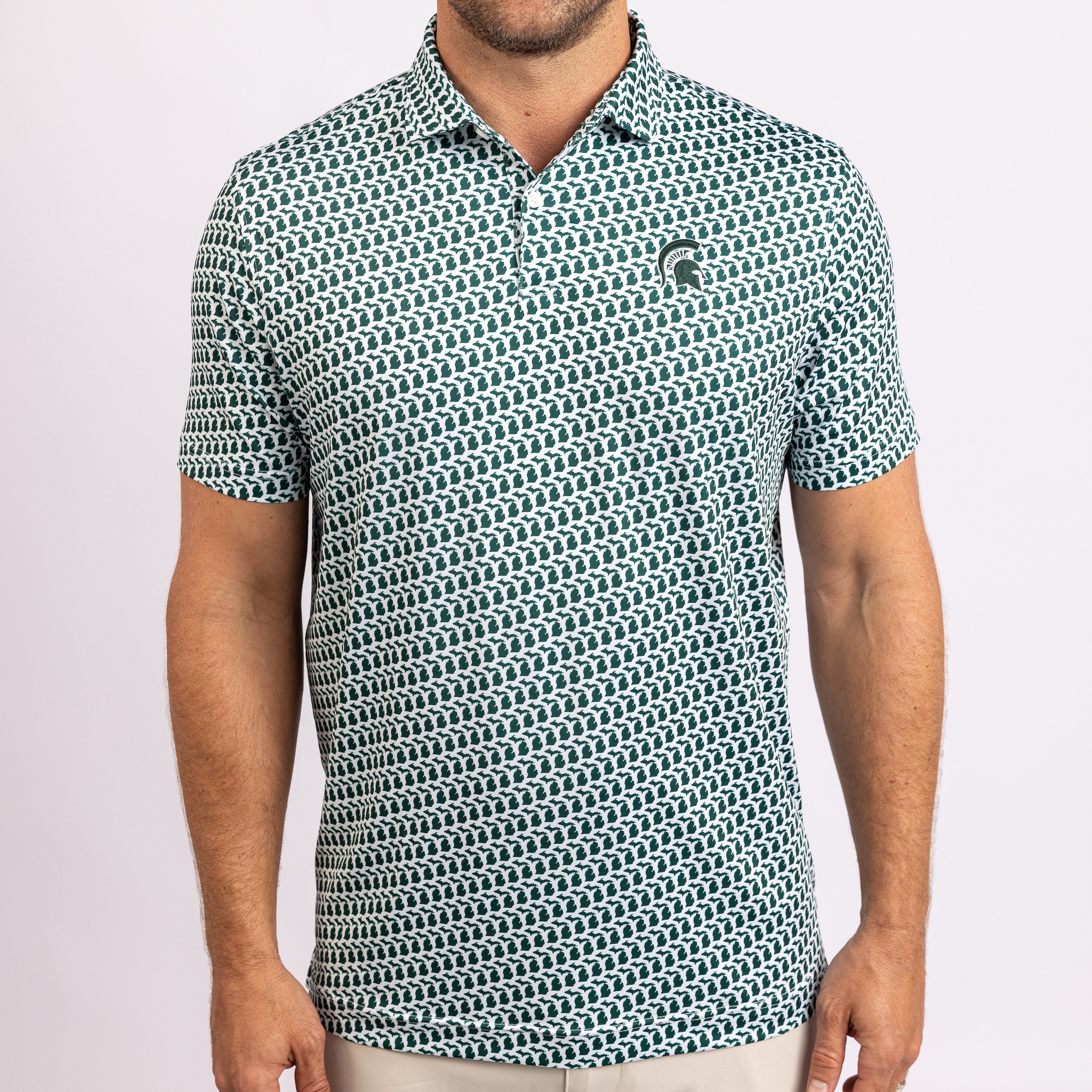 A man wearing a short-sleeve polo shirt with a repeating geometric pattern in teal and white, featuring a small embroidered Spartan helmet logo on the left chest.