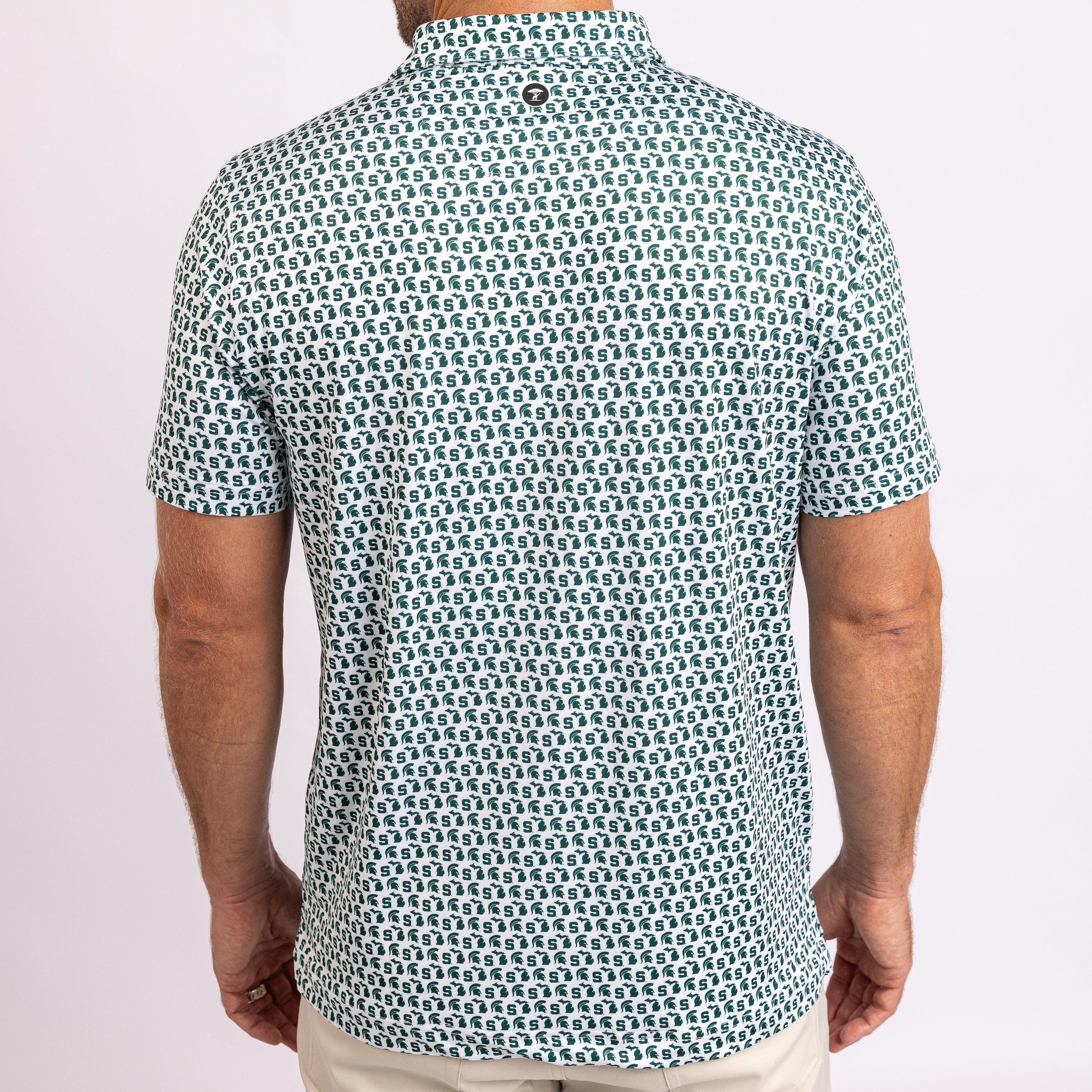 A man viewed from the back wearing a short-sleeve button-up shirt with an all-over repeating geometric pattern in teal and off-white, paired with light beige pants against a plain light background.