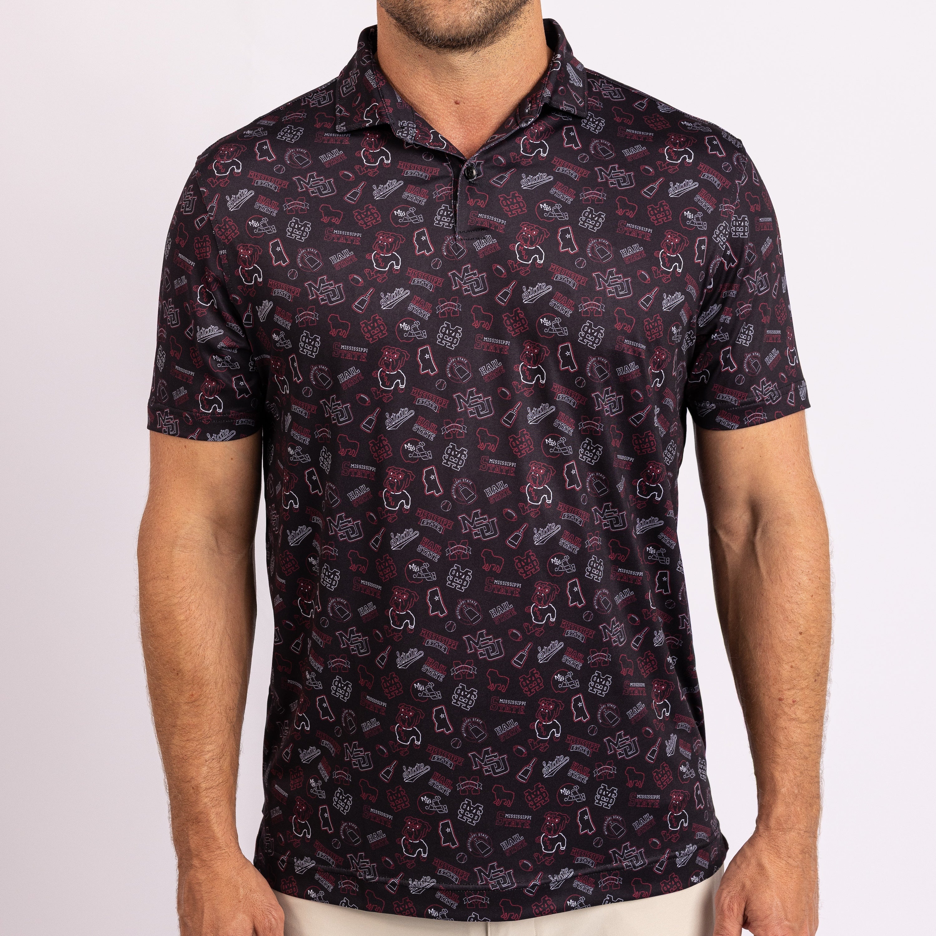 A man wearing a short-sleeve polo shirt with an all-over retro gaming controller pattern in dark red, gray, and white on a black base, photographed against a light gray studio background.