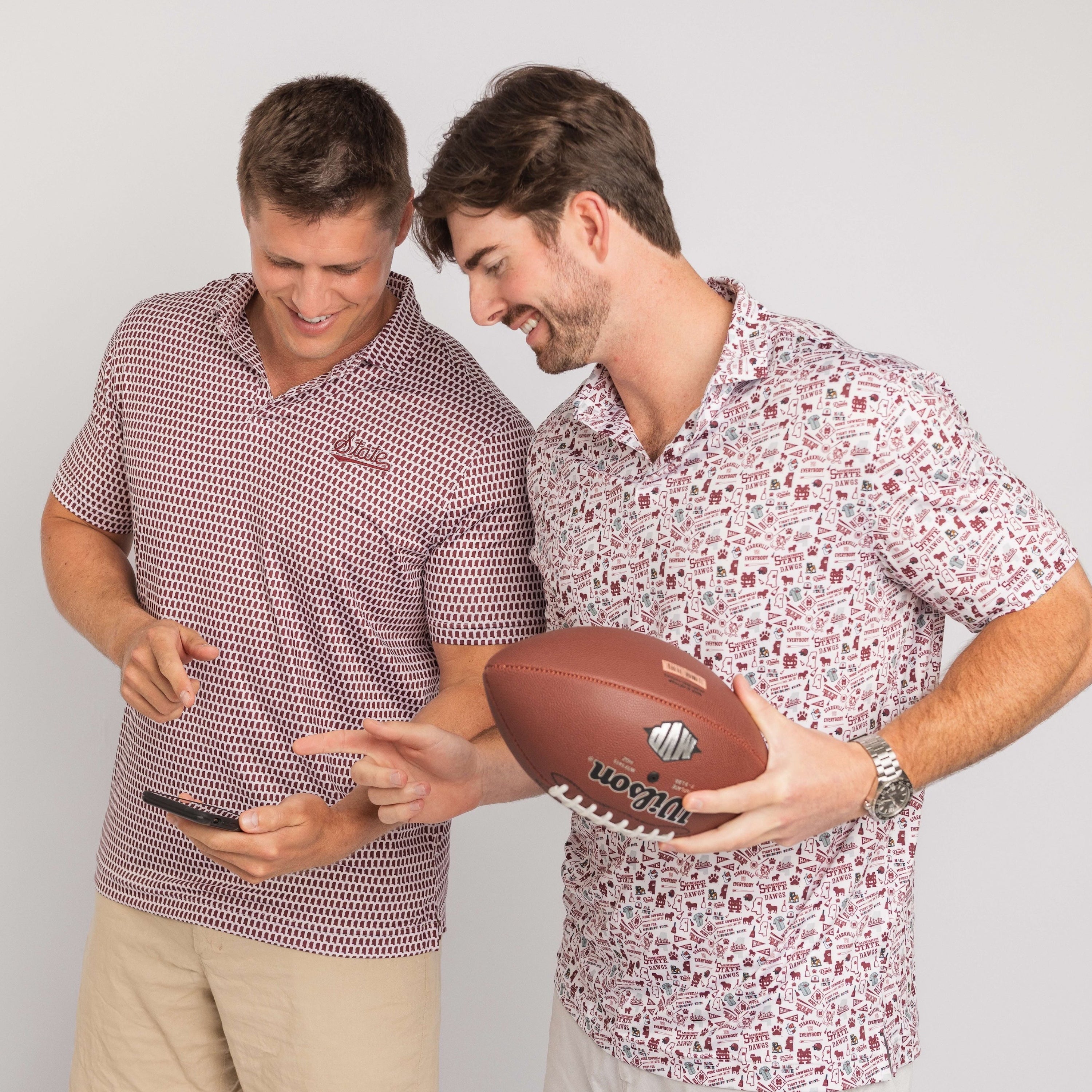 Two men wearing patterned shirts holding a football against a plain background