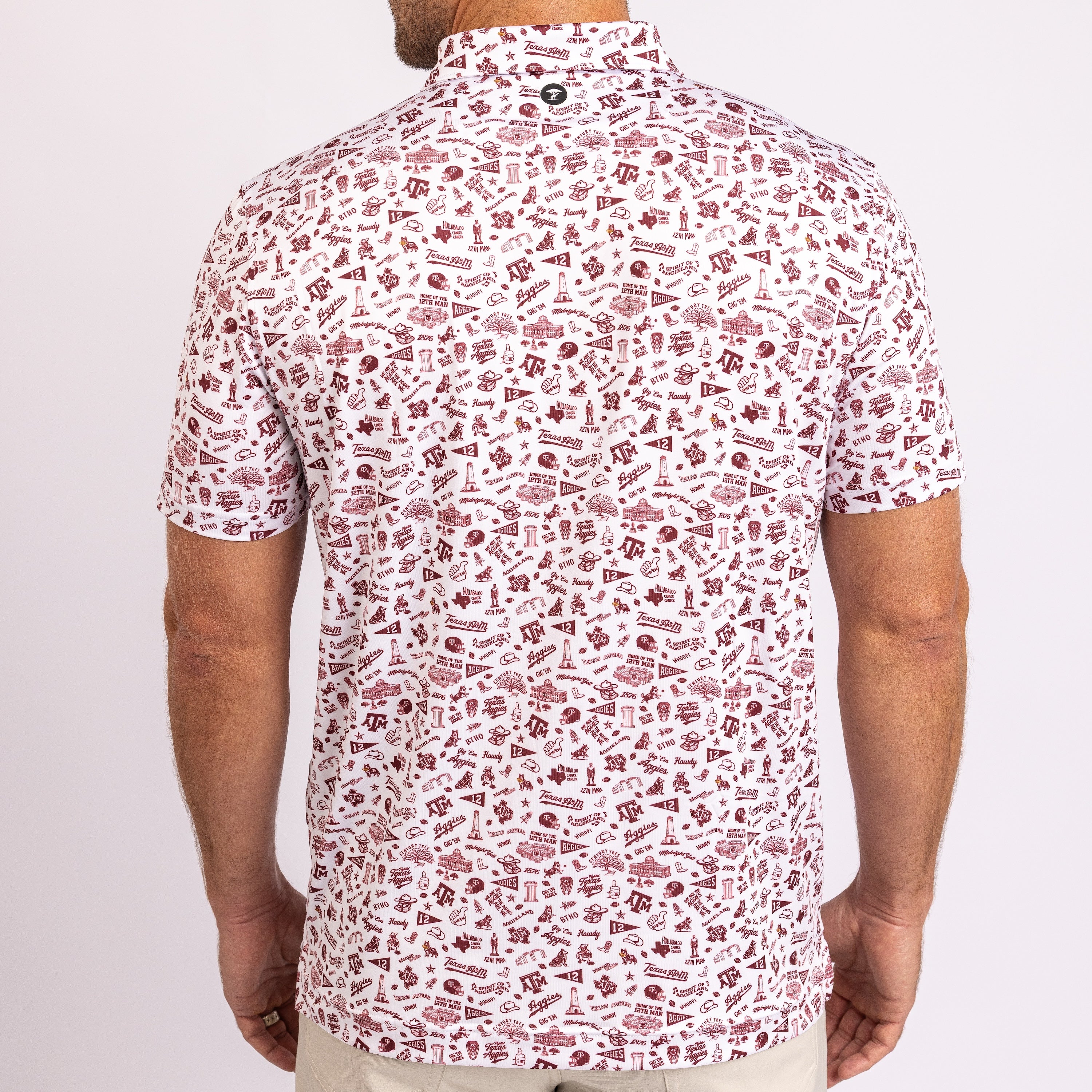 A man viewed from the back wearing a short-sleeve button-up shirt with an all-over maroon and white novelty print of small icons and text, paired with light beige pants against a plain light background.