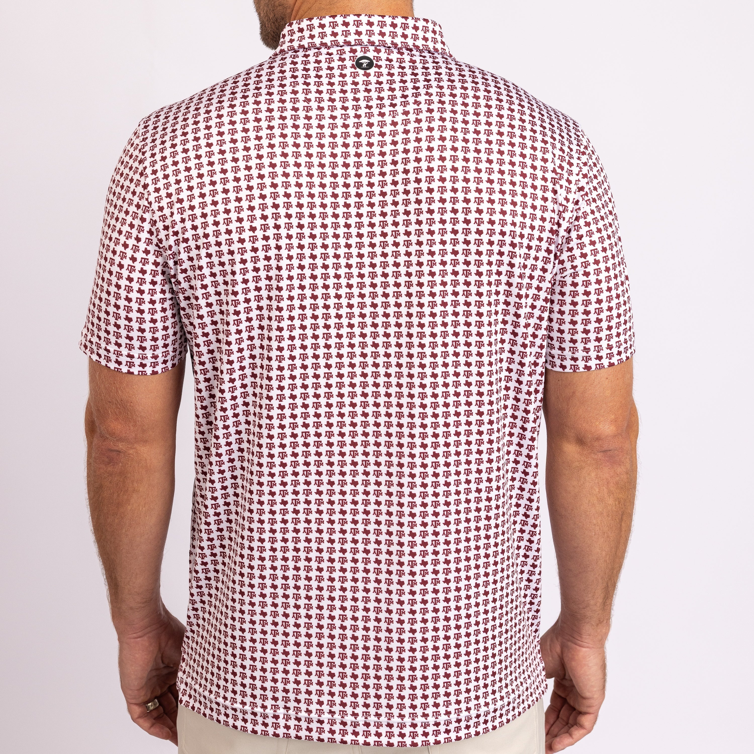 A man viewed from the back wearing a short-sleeve polo shirt with a dense small-scale red and white geometric pattern, paired with light beige pants against a plain white studio background.