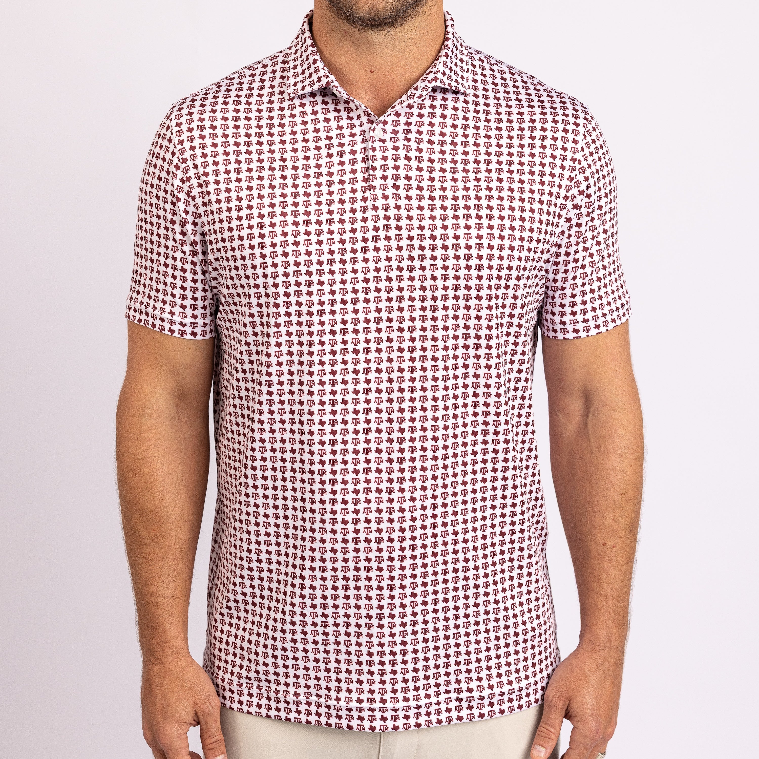 A man wearing a short-sleeve polo shirt with a dense repeating geometric pattern in dark red/burgundy and off-white, paired with light beige trousers, shot against a plain light background.