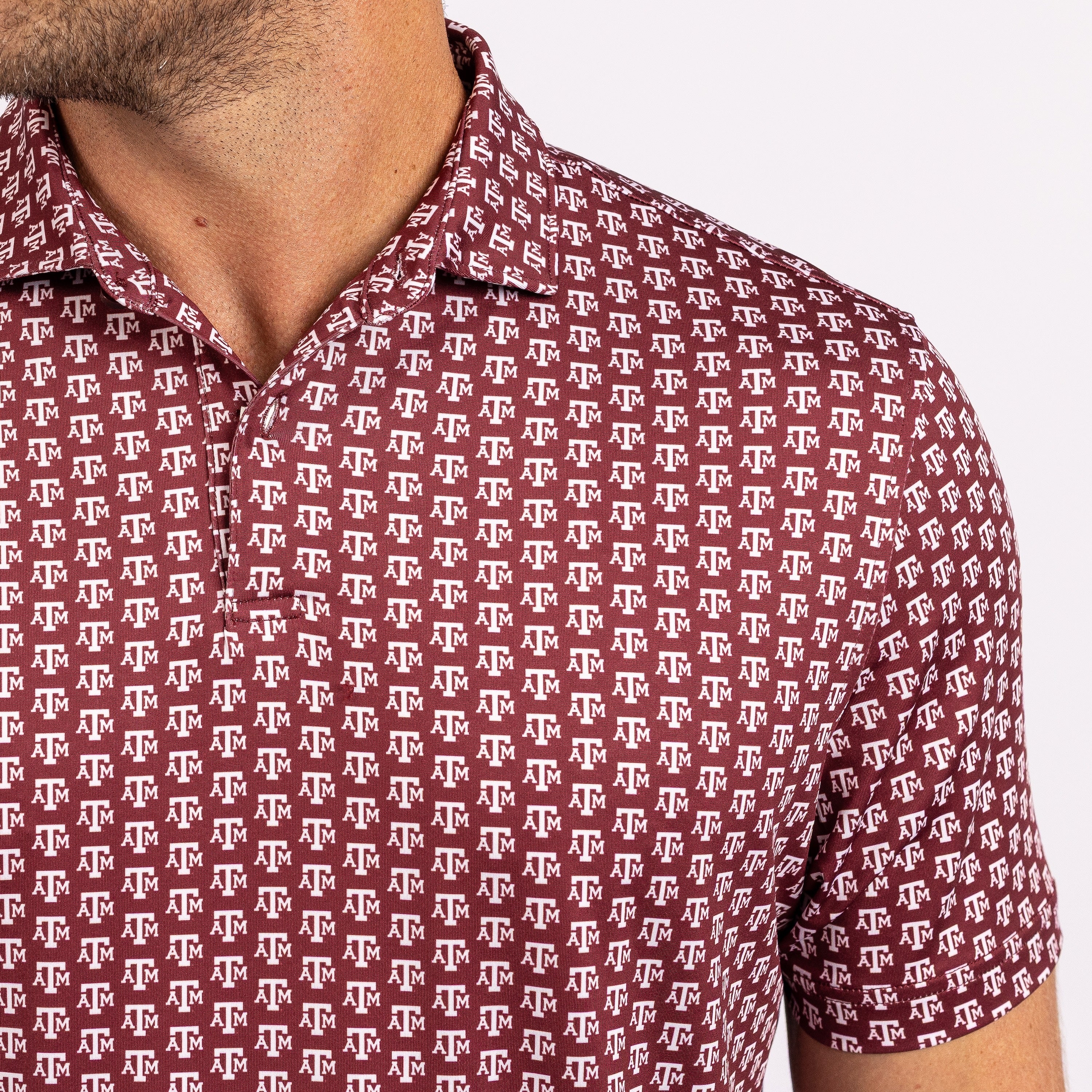 Close-up of a man wearing a short-sleeve collared polo shirt with an allover maroon and white Texas A&M Aggies logo pattern.