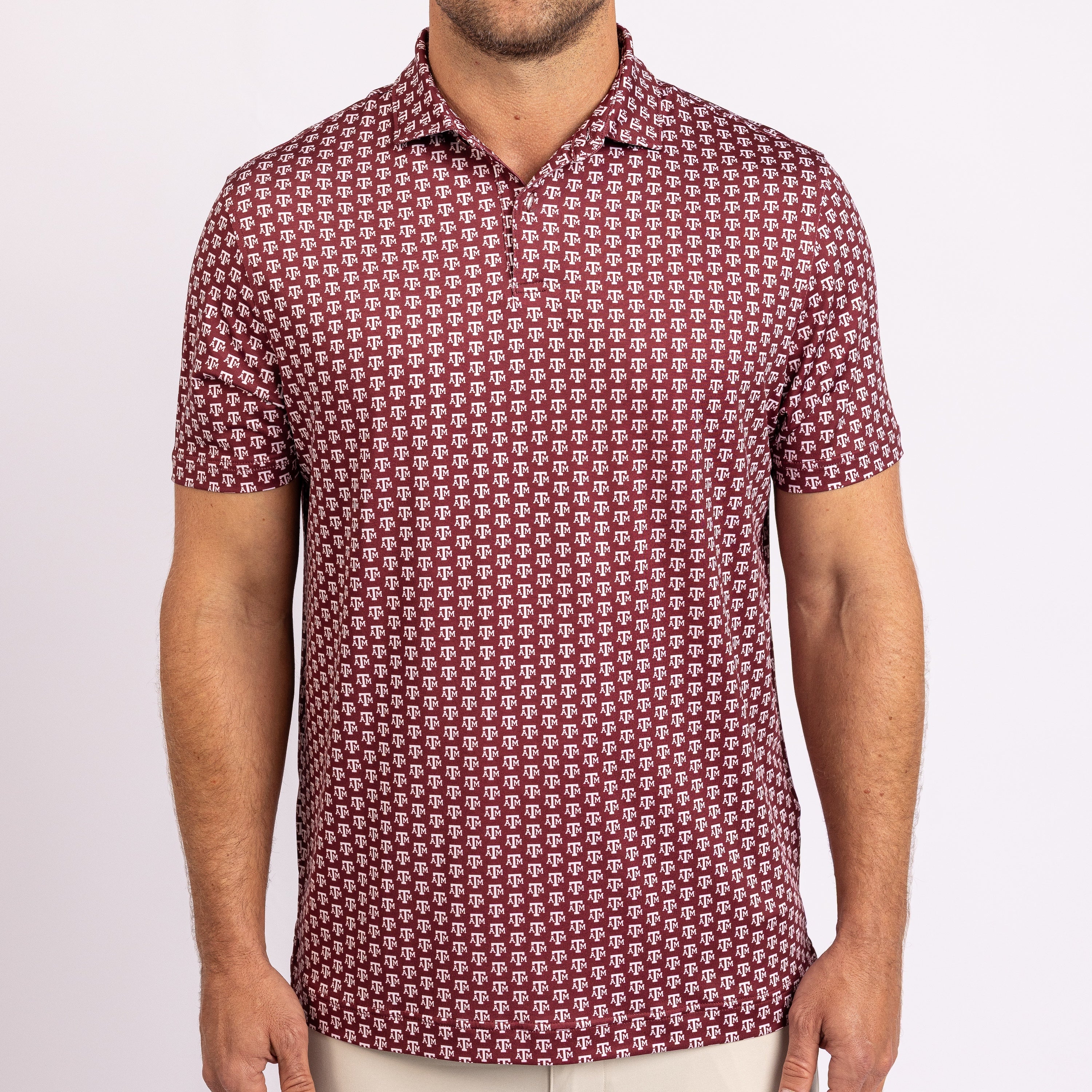 A man wearing a short-sleeve polo shirt with a repeating geometric pattern in burgundy and white, paired with light beige pants, against a plain light gray background.
