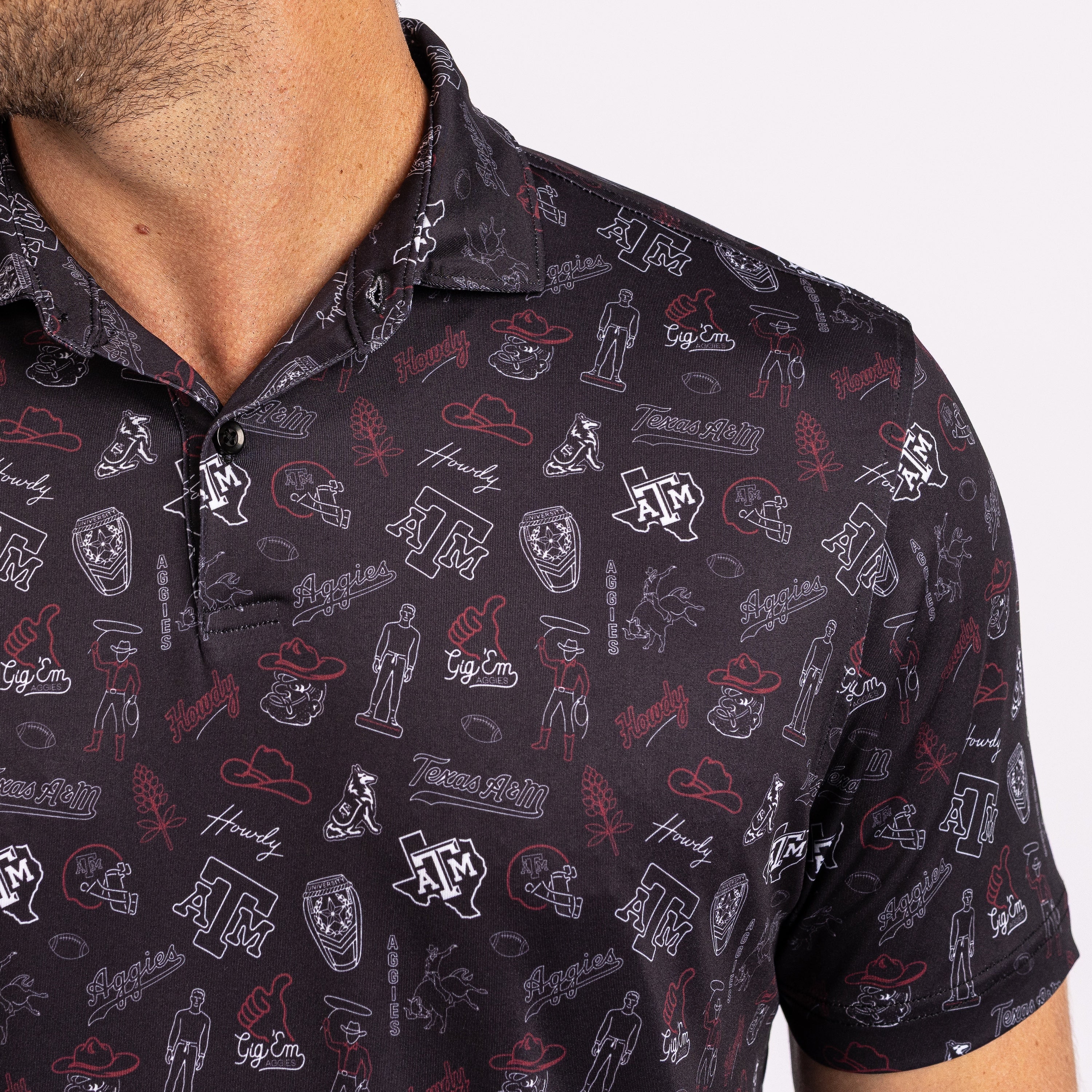 A close-up of a man wearing a short-sleeve polo shirt with an all-over Texas A&M University themed print. The shirt features white and red graphics including the 'A&M' logo