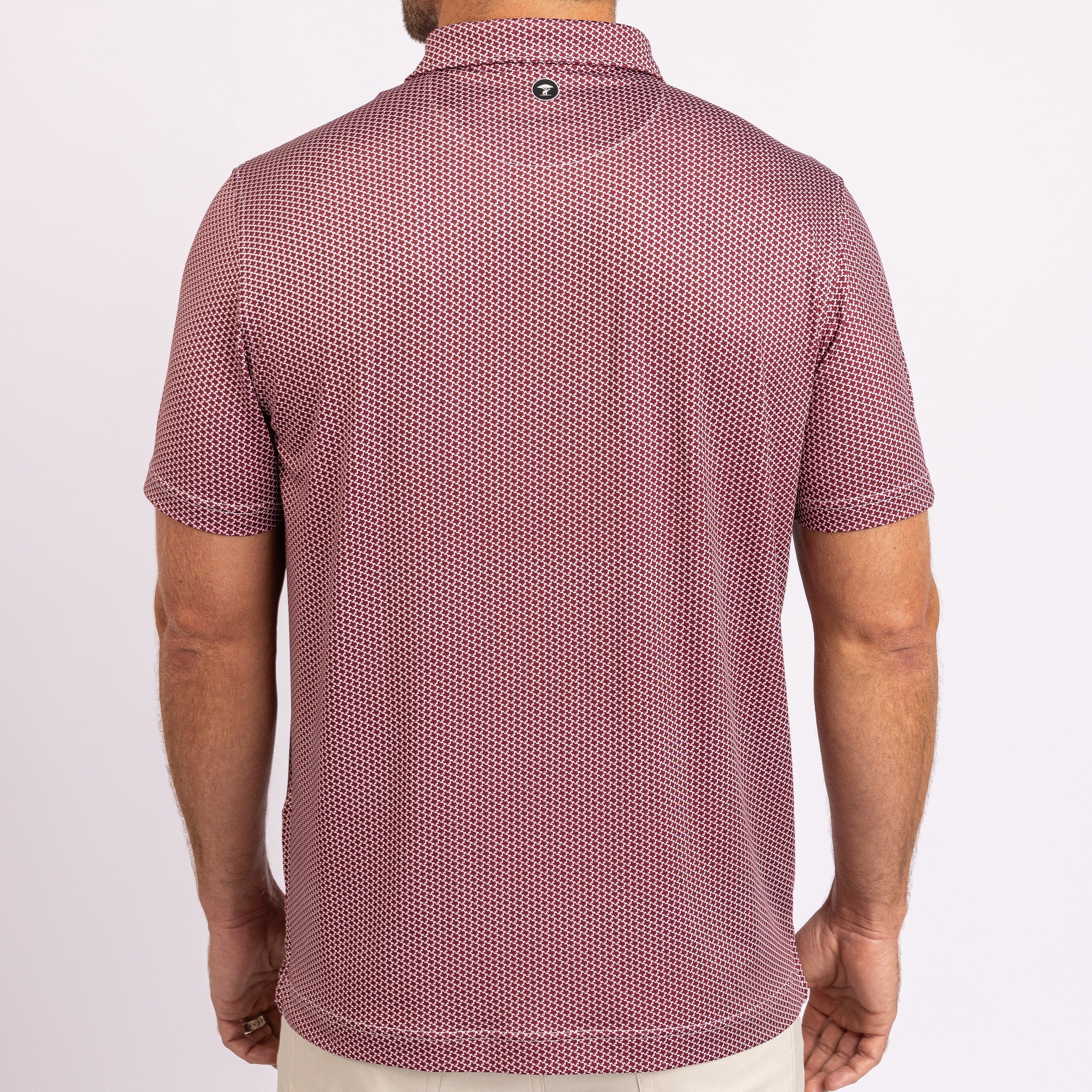 Rear view of a man wearing a short-sleeve polo shirt with a textured micro-dot pattern in dusty rose and white, paired with light beige pants, against a plain white background.