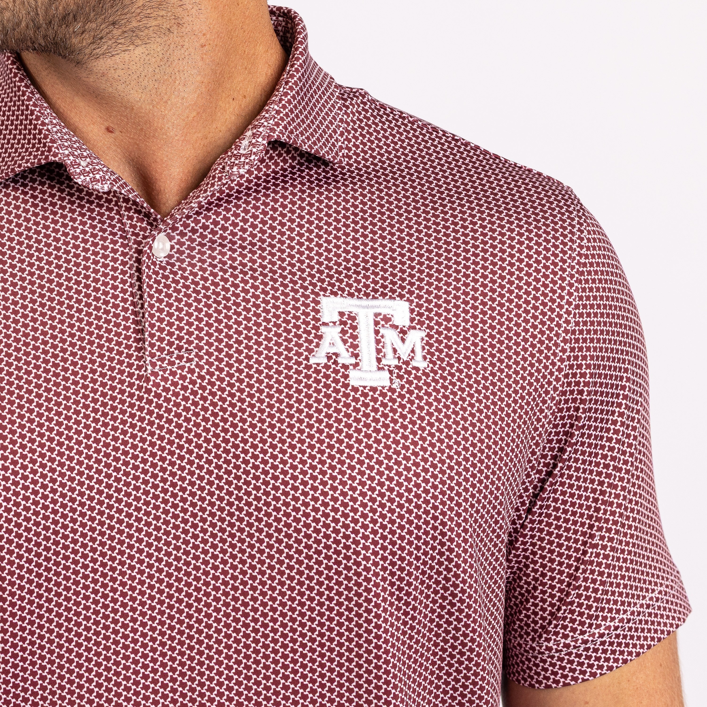 Close-up of a man wearing a short-sleeve polo shirt with a maroon and white geometric pattern and a white Texas A&M 'A&M' logo on the left chest.
