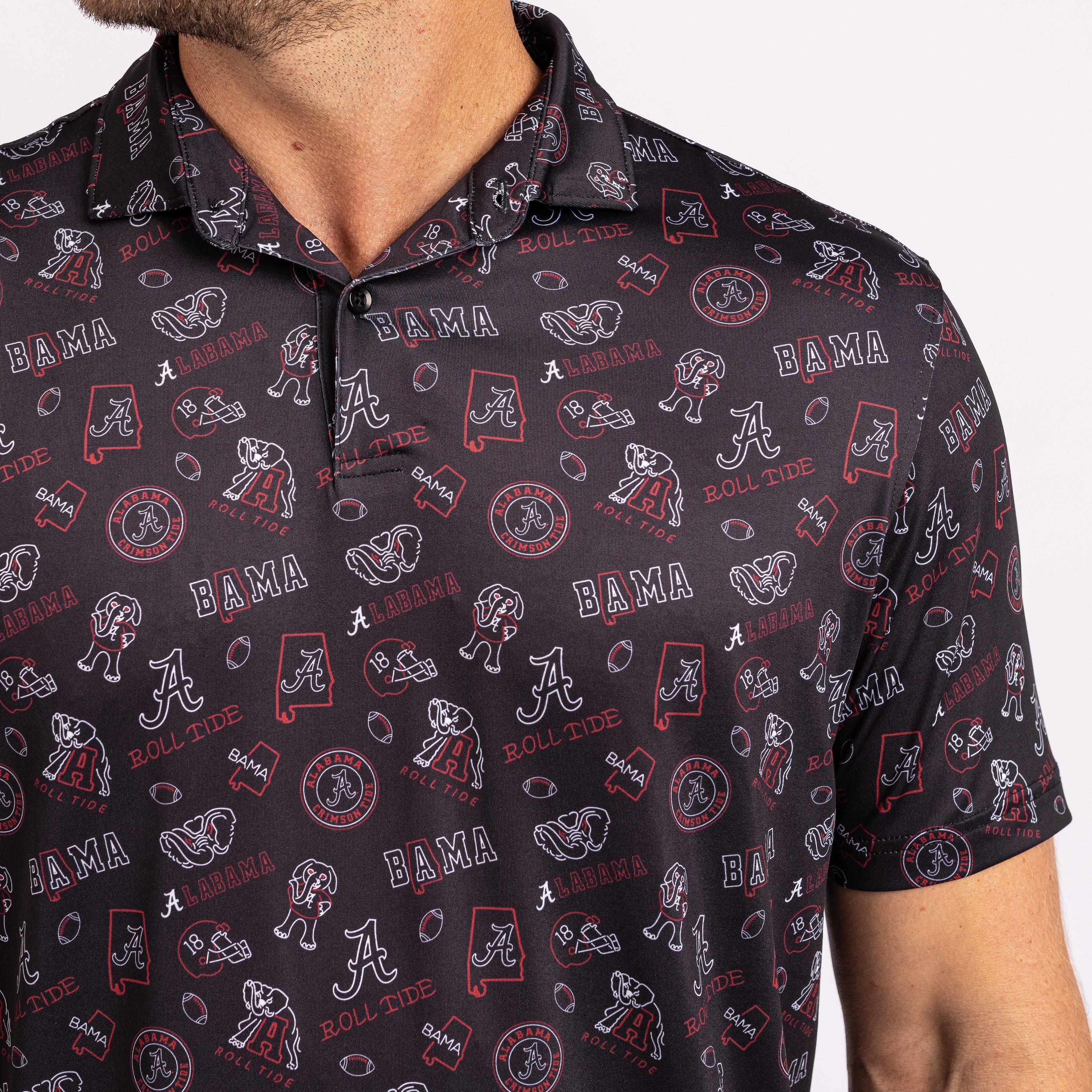 A close-up of a man wearing a short-sleeve polo shirt with an all-over Alabama Crimson Tide themed print. The shirt features white and red graphics including the 'A' logo, 'BAMA' text, footballs, and state silhouettes on a dark charcoal background.