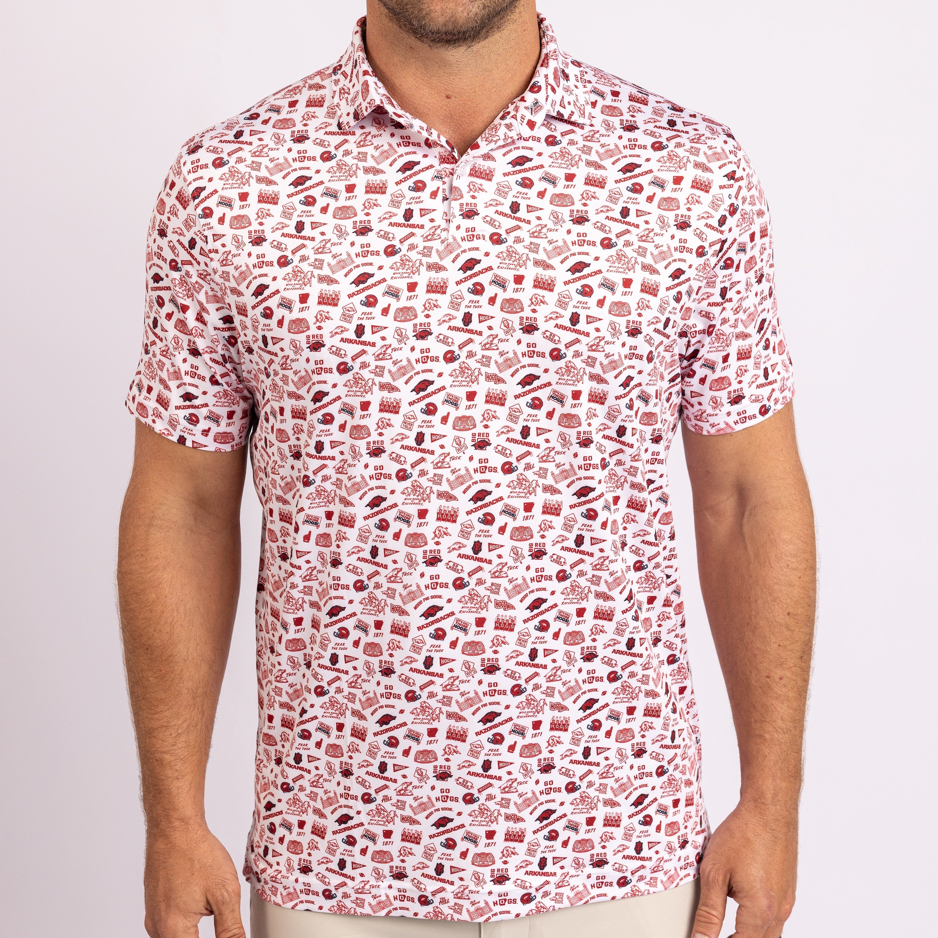 A man wearing a short-sleeve polo shirt with a dense red and brown graphic pattern on a white background, shown from the neck down against a light gray studio backdrop.
