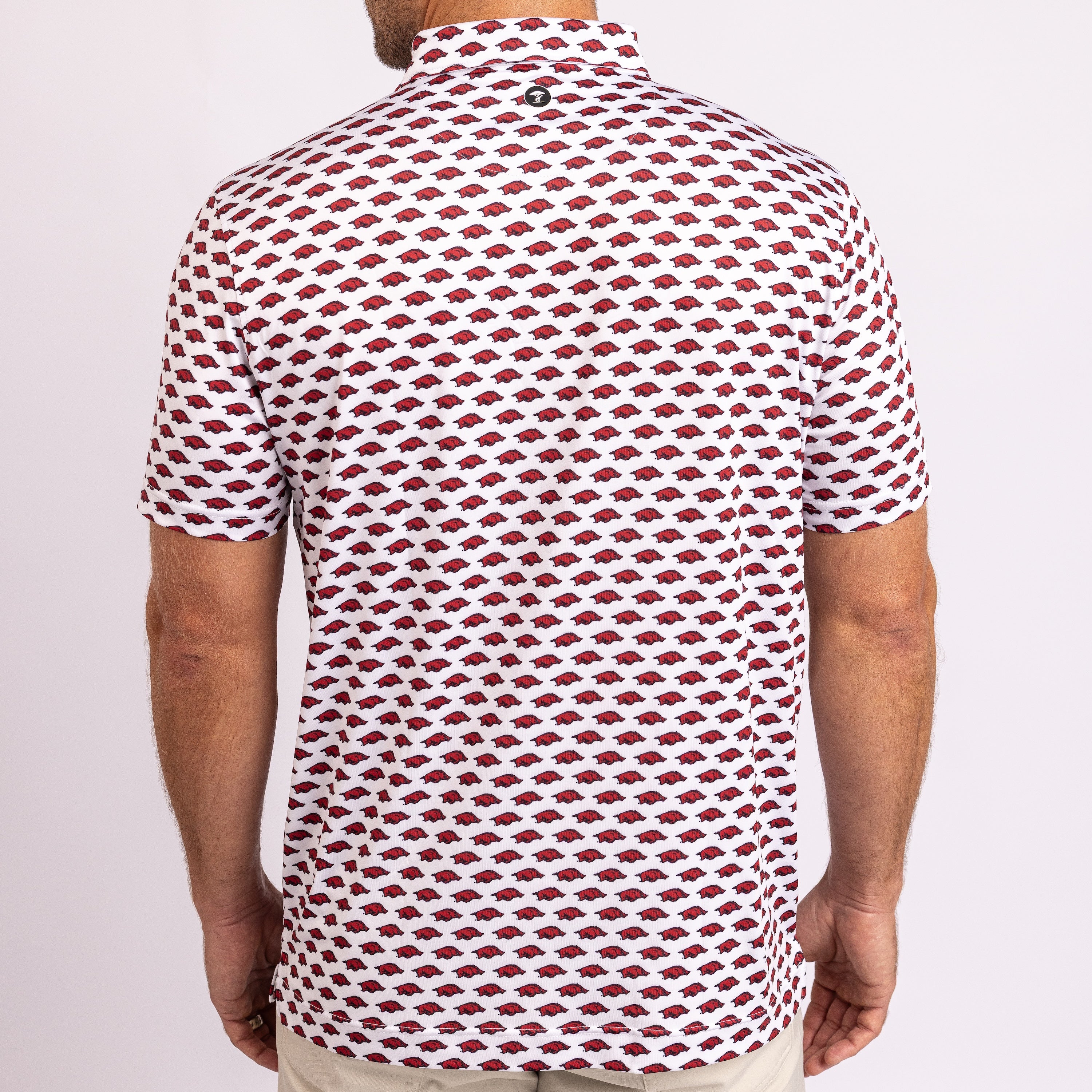 A man viewed from the back wearing a short-sleeve polo shirt with a repeating red and white geometric pattern, paired with light beige pants, against a plain white background.