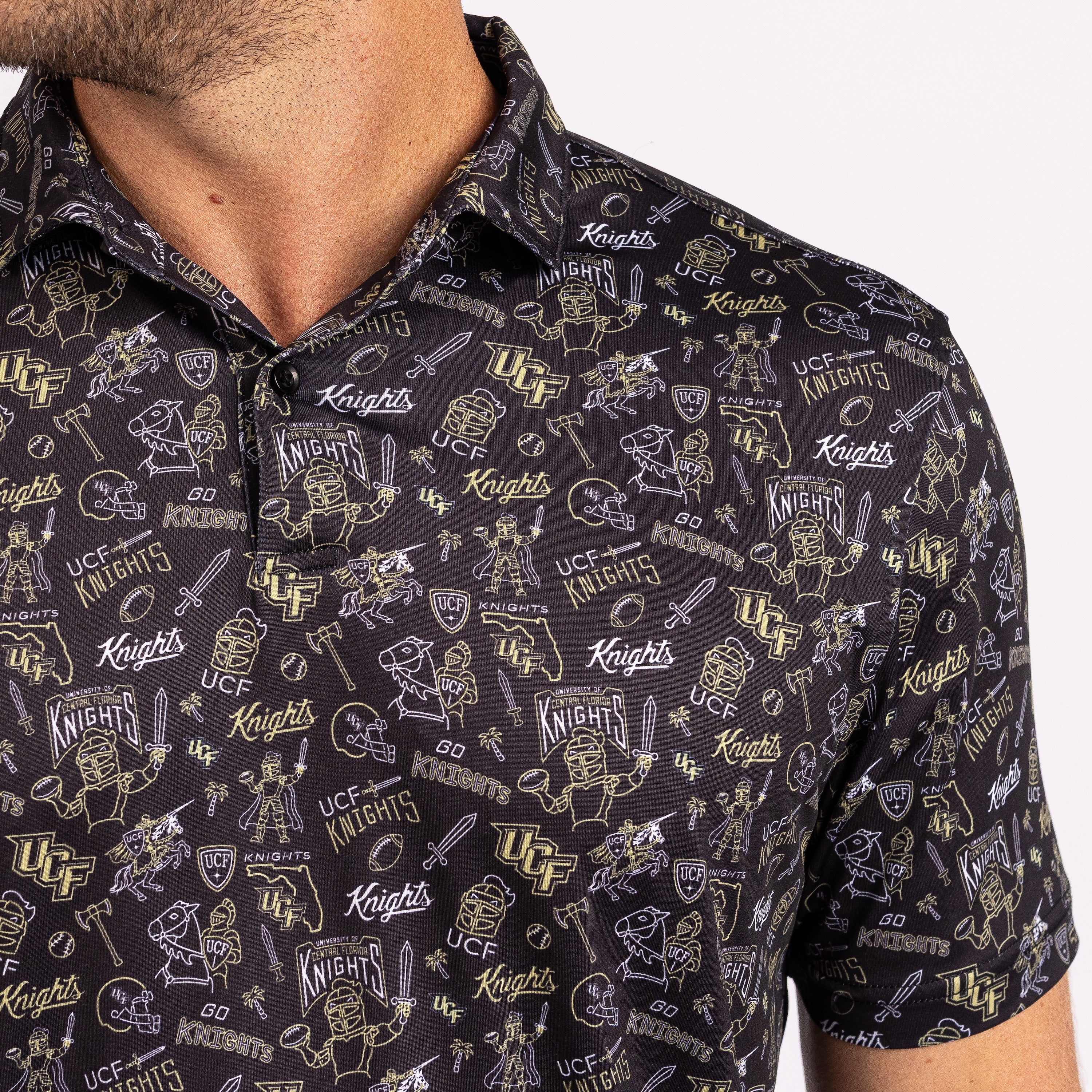 A close-up of a man wearing a short-sleeve button-up shirt with an all-over UCF Knights graphic print in gold and white on a black background.