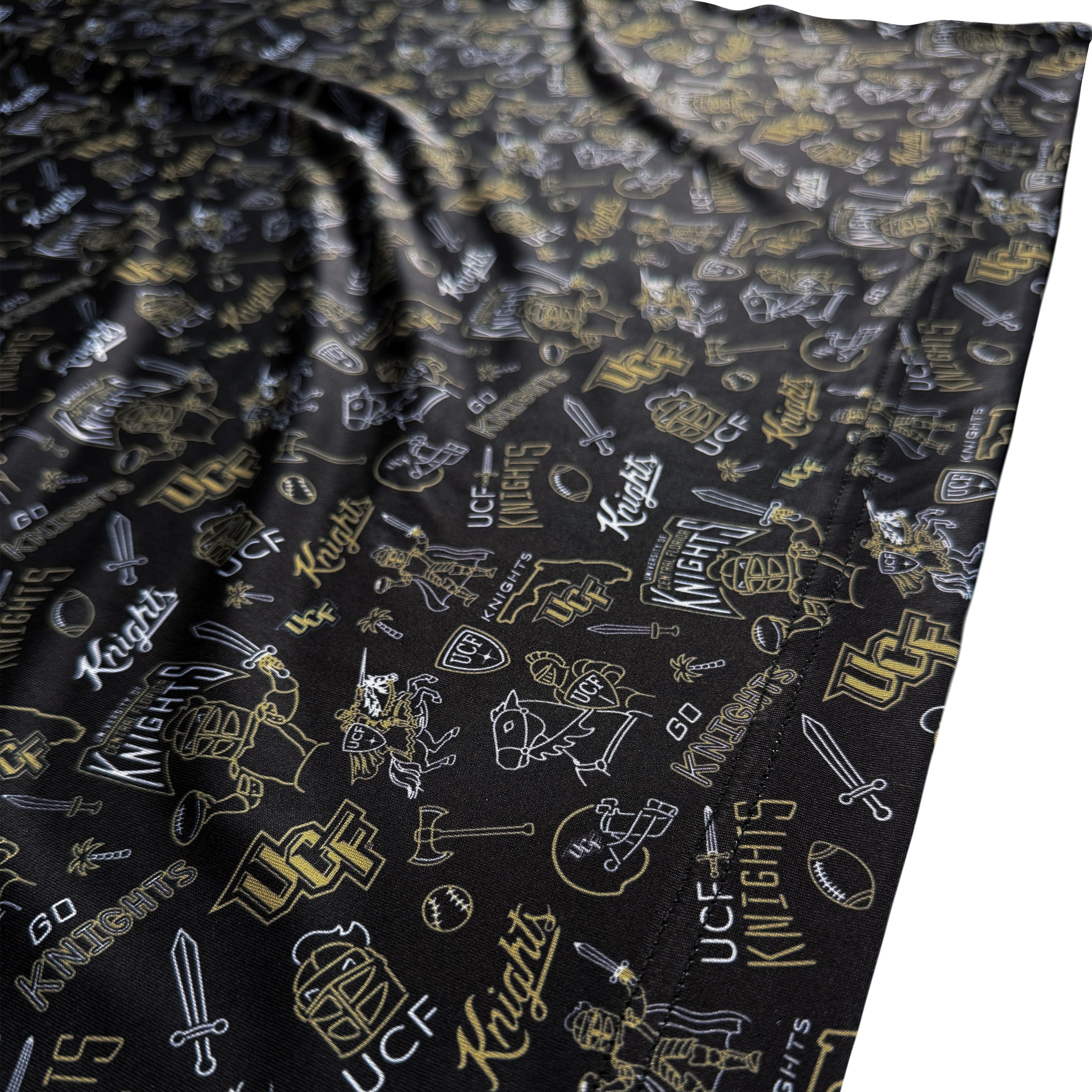 A close-up of a black fabric product, likely a towel or blanket, featuring a repeating gold and white outline pattern of UCF Knights logos, symbols, and text.
