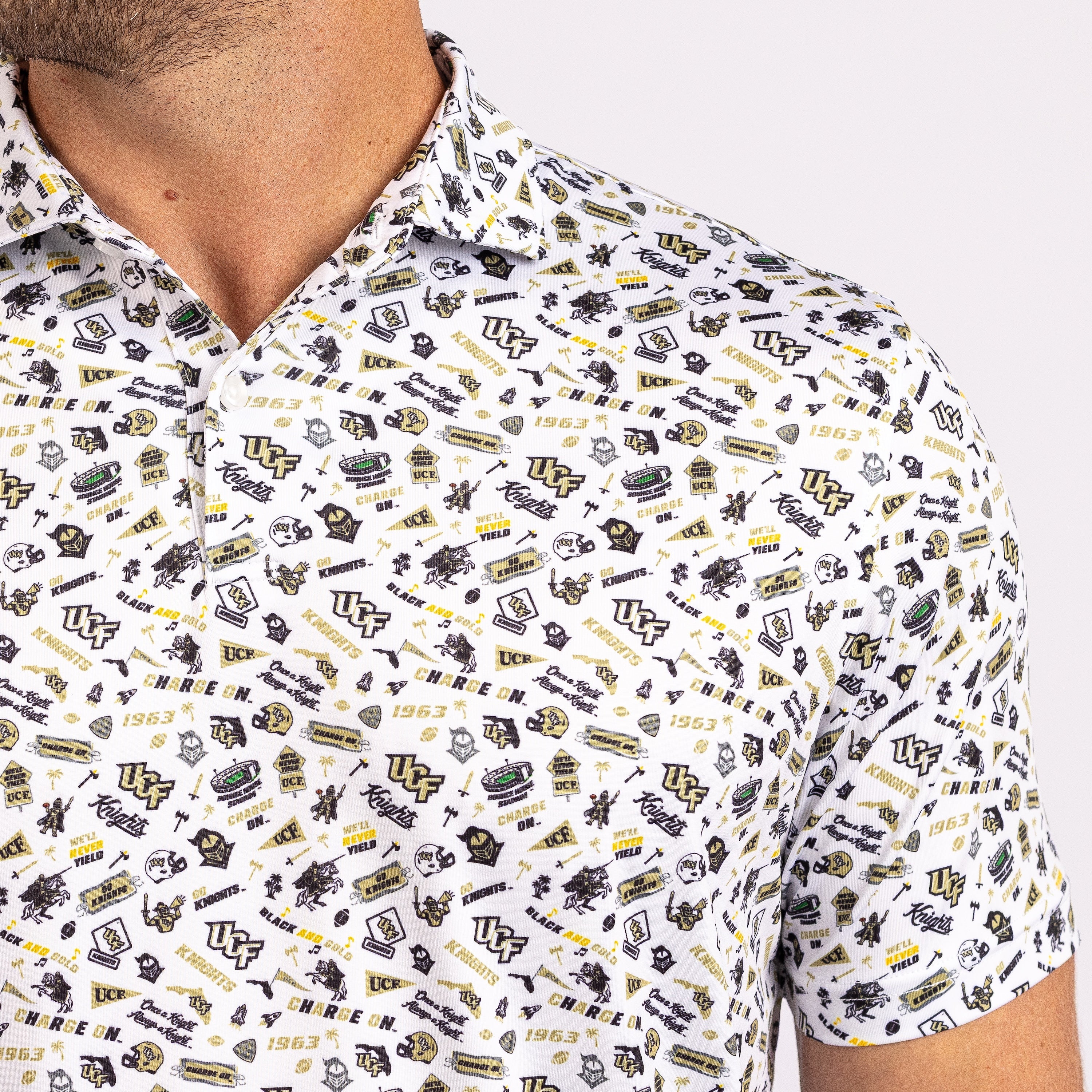 A close-up of a man wearing a white short-sleeve collared shirt with an all-over collegiate-style print in black and yellow.