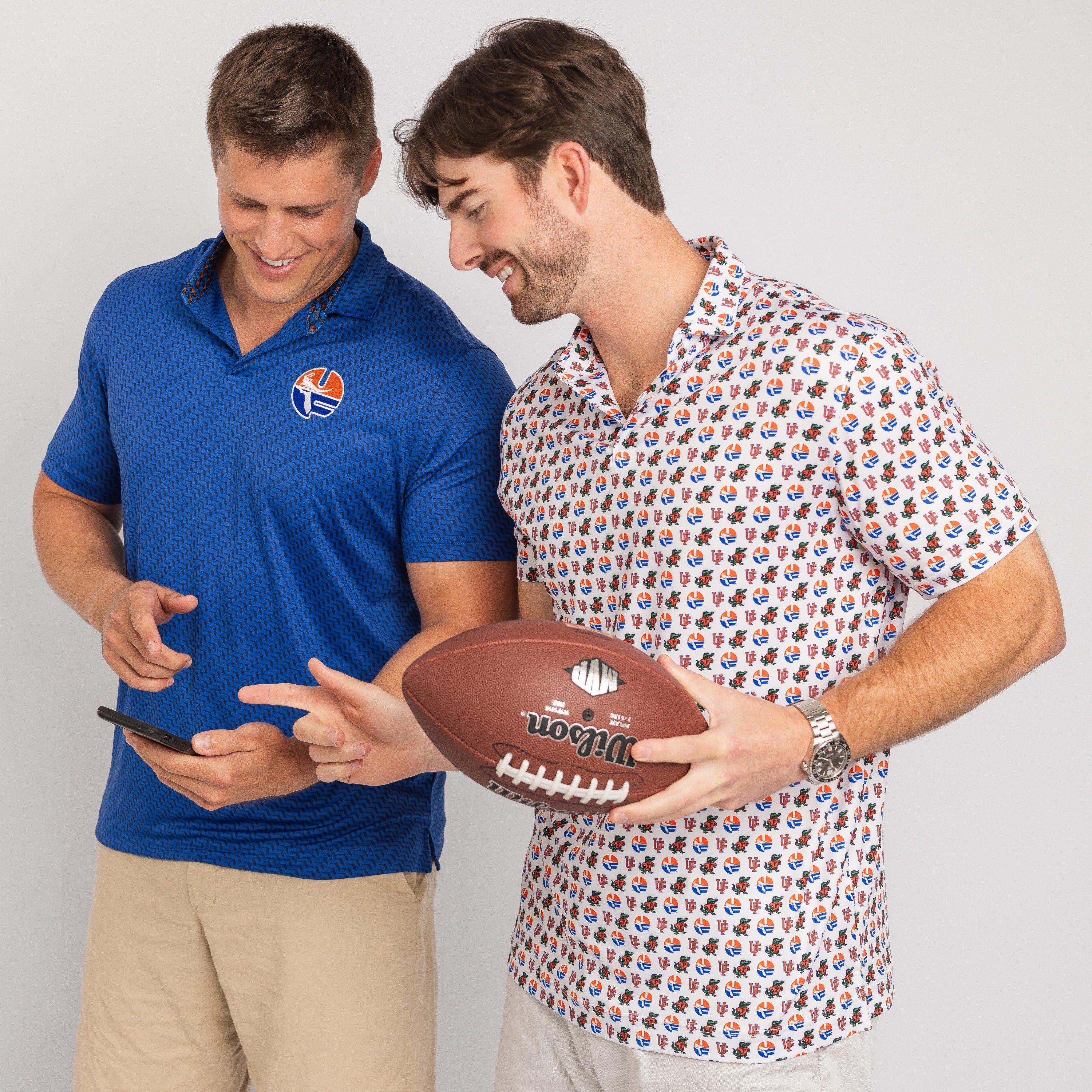 Two men, one holding a football and the other looking at a phone, on a plain background
