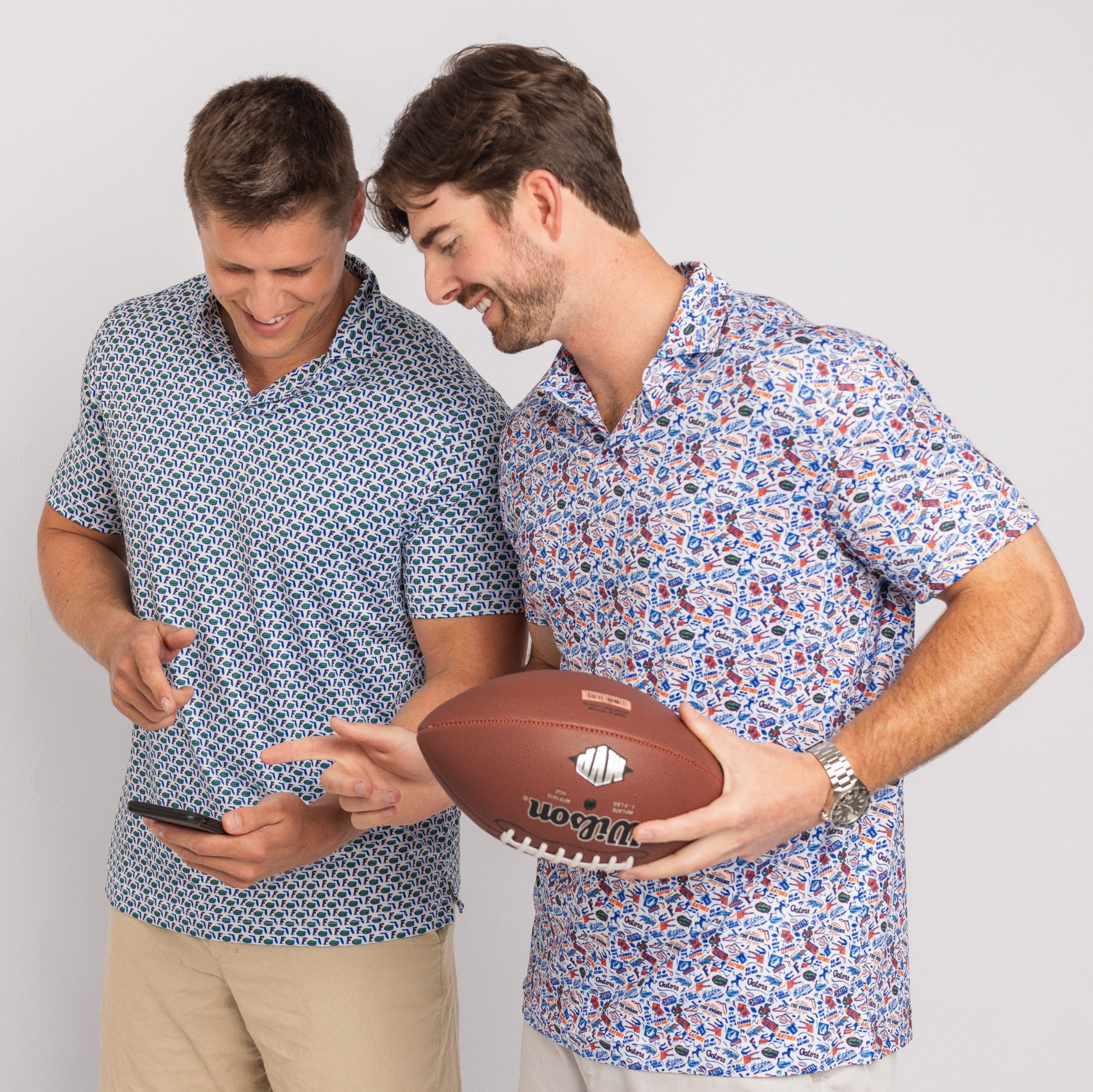 Two men wearing patterned shirts holding a football and a phone on a plain background