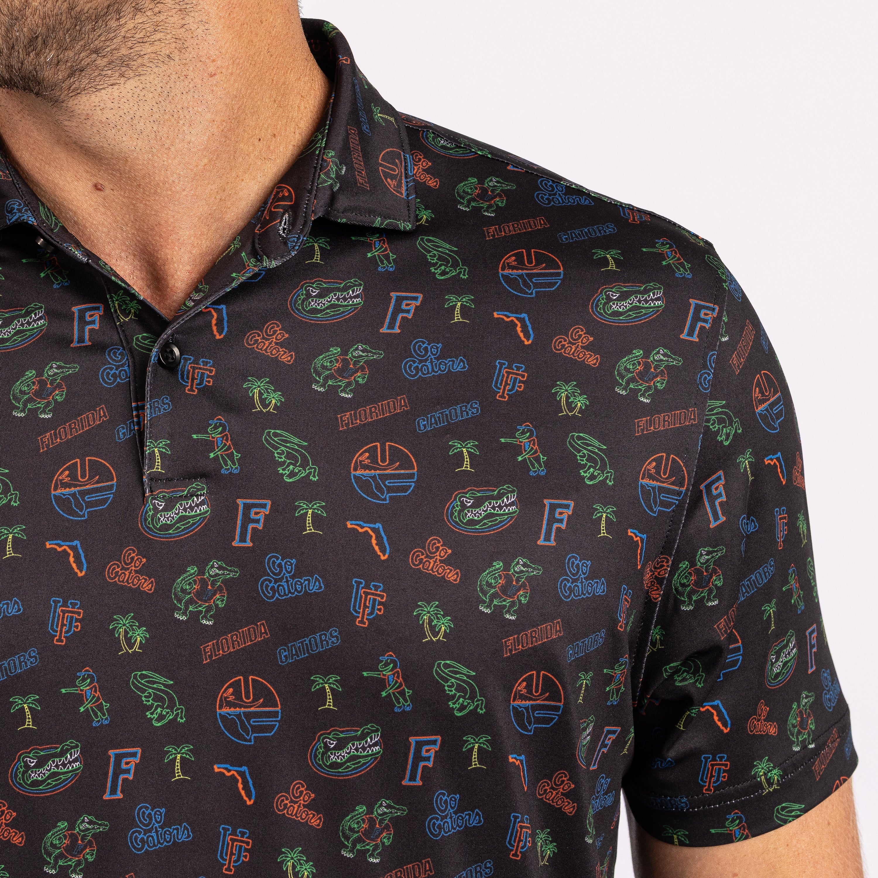 A close-up of a man wearing a black short-sleeve polo shirt with an all-over Florida Gators themed print featuring the team name, logos, and green alligator illustrations.