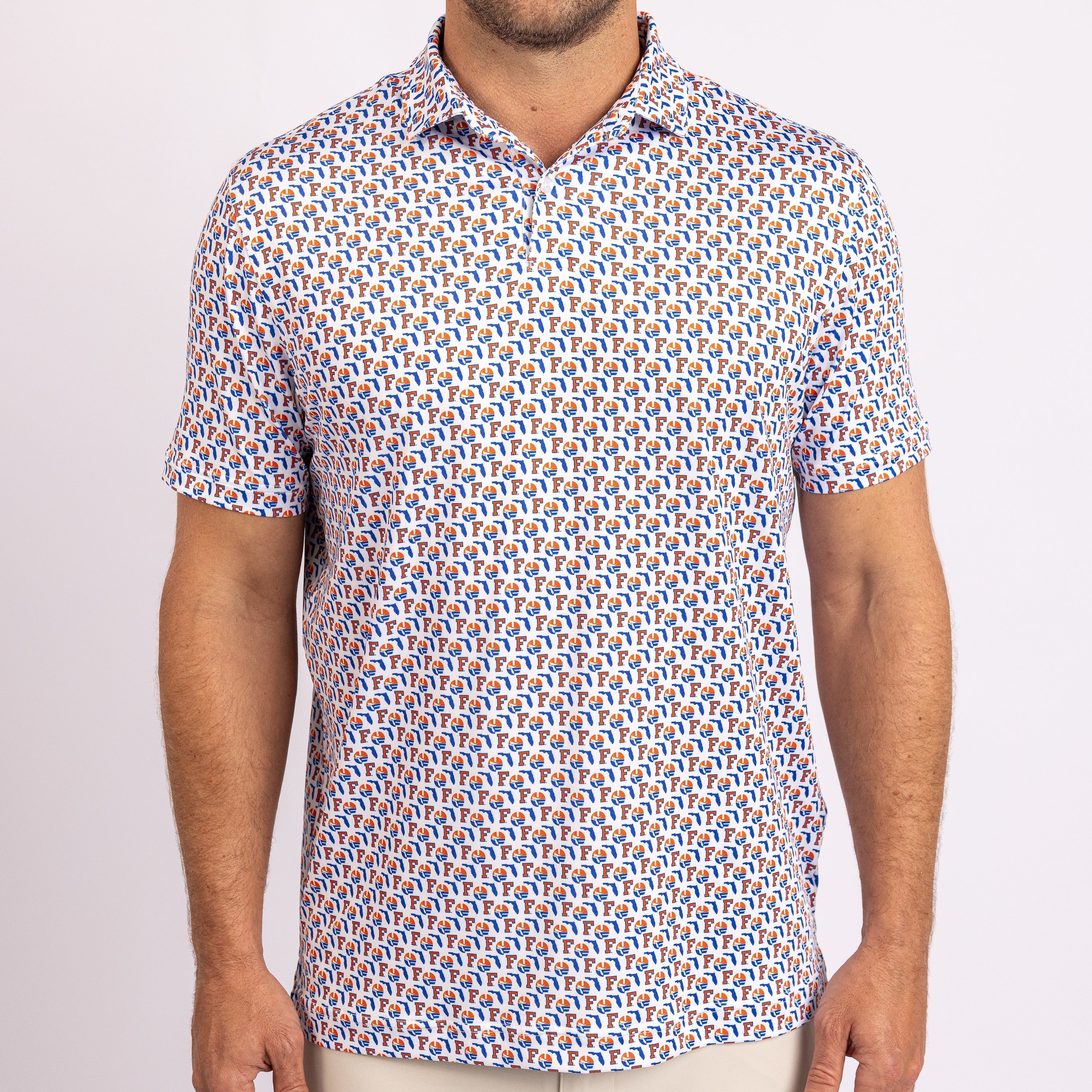 A man wearing a short-sleeve polo shirt with a dense repeating geometric pattern in blue, orange, and white, paired with light beige trousers against a plain light background.