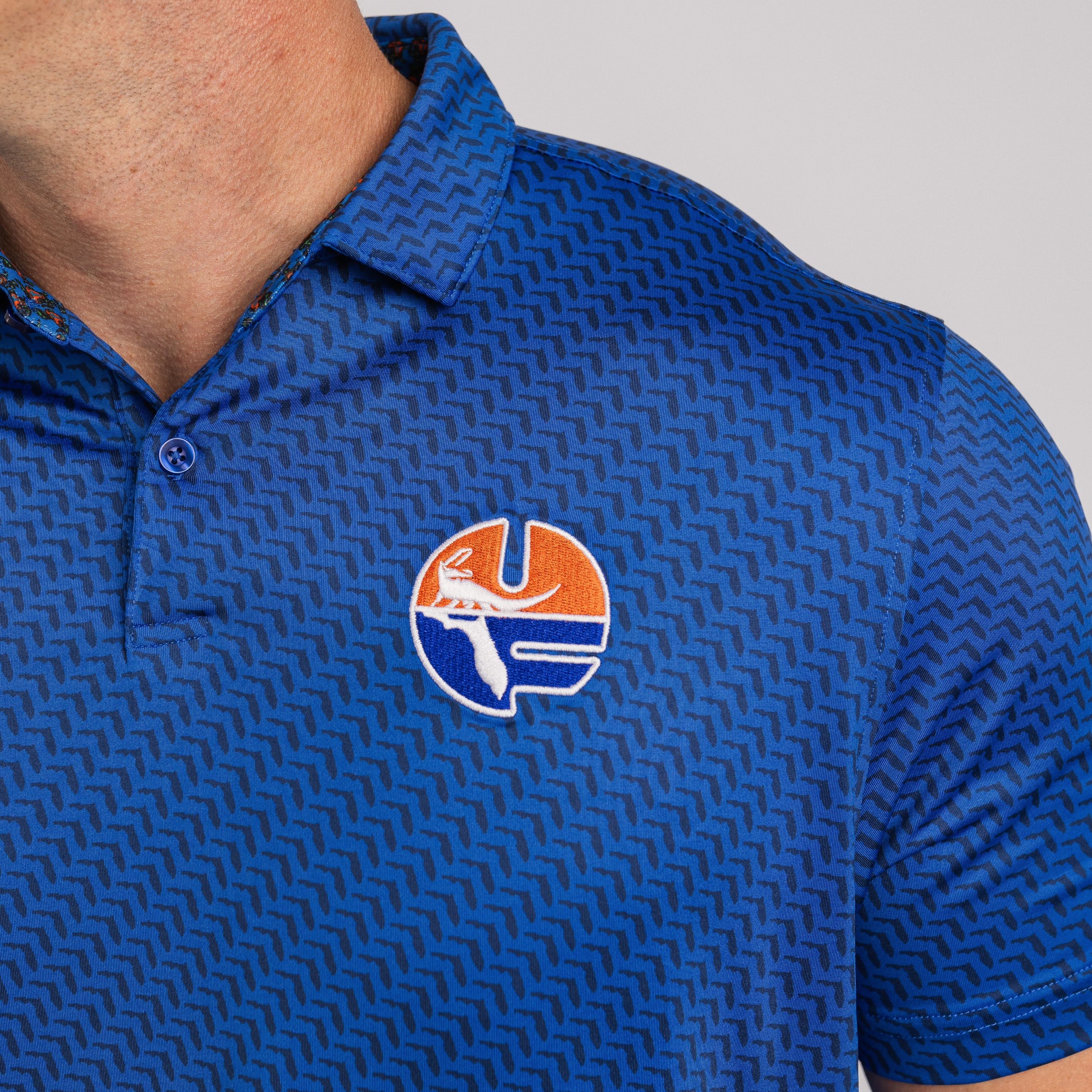 Blue patterned polo shirt with a logo on the chest against a gray background