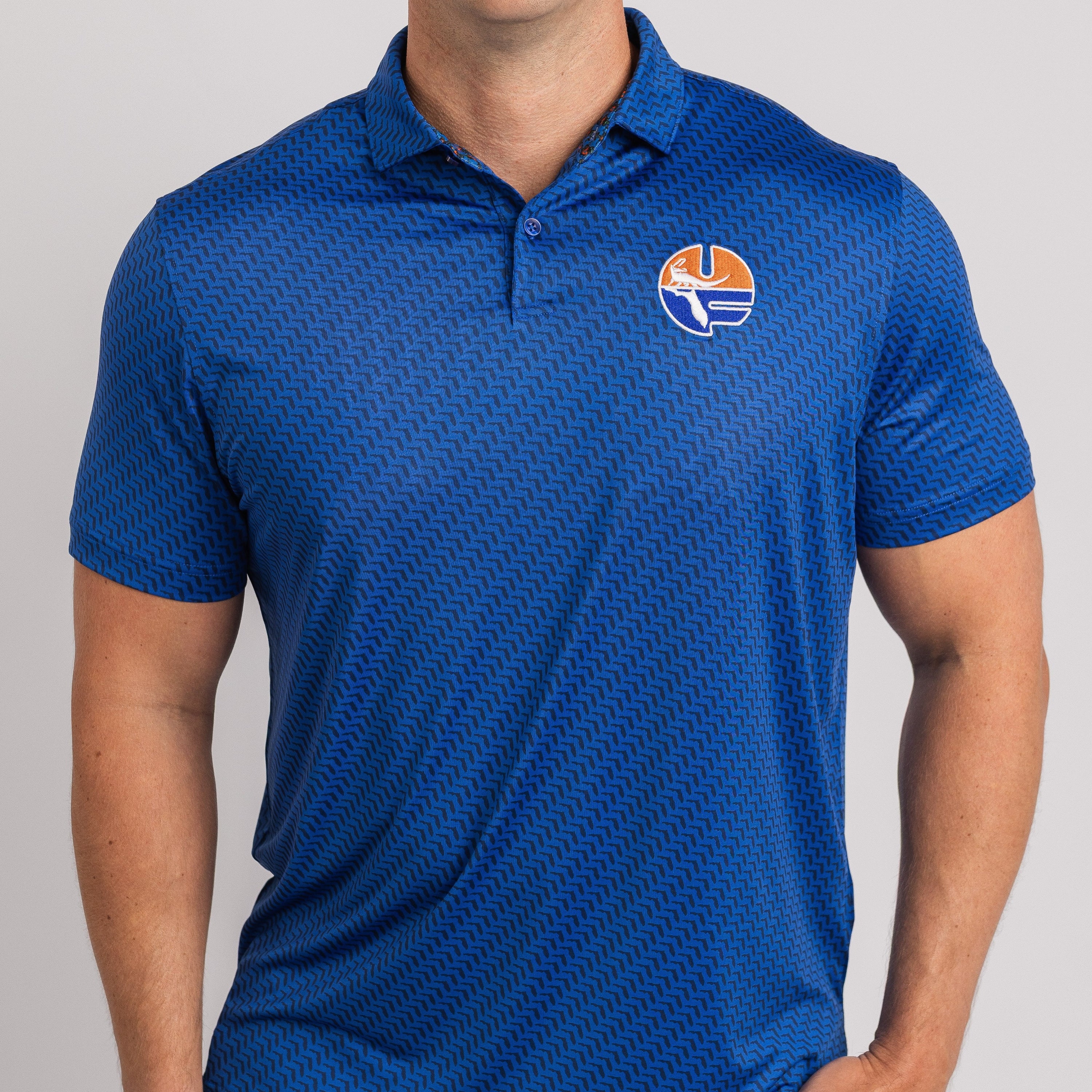 Man wearing a blue patterned polo shirt with a logo on a gray background
