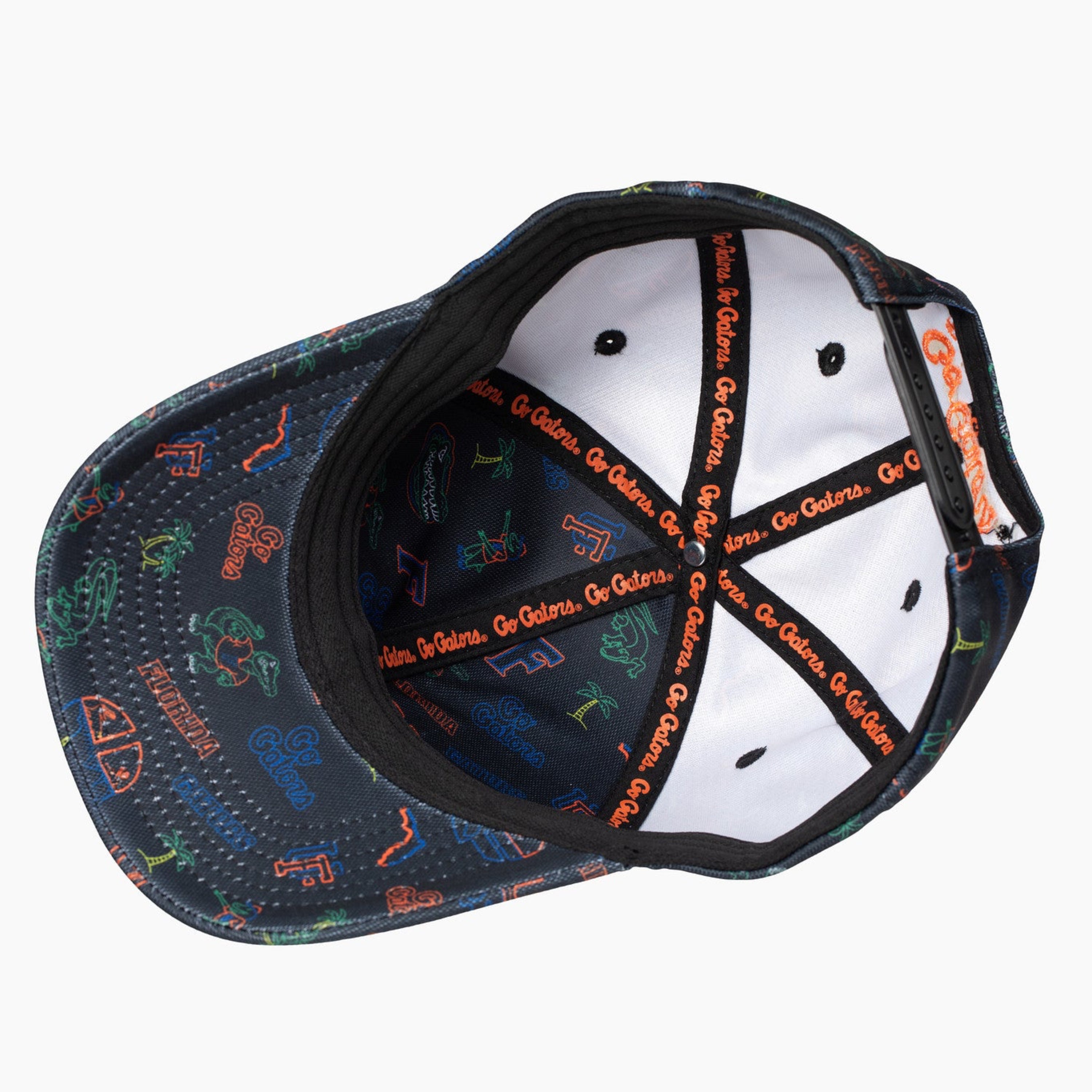 An overhead view of a baseball cap's interior, showing a black brim with a colorful graphic print, a white structured crown, and black adjustable straps with orange text.