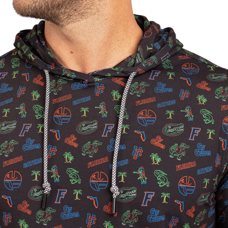 Close-up of a person wearing a dark charcoal hoodie with an all-over Florida Gators graphic print in green, orange, and blue, featuring white drawstrings.