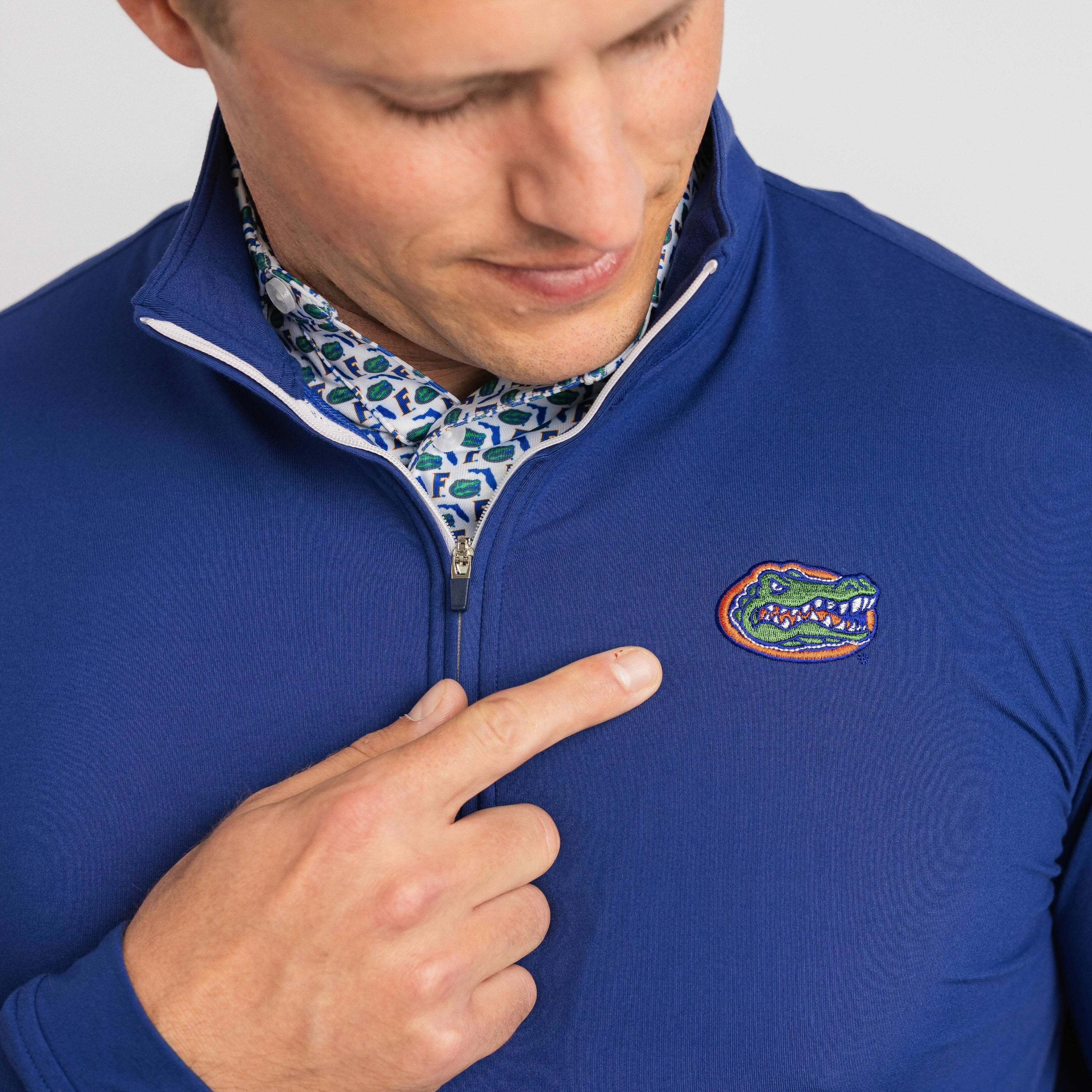 Man wearing a blue pullover with a logo, pointing to it.
