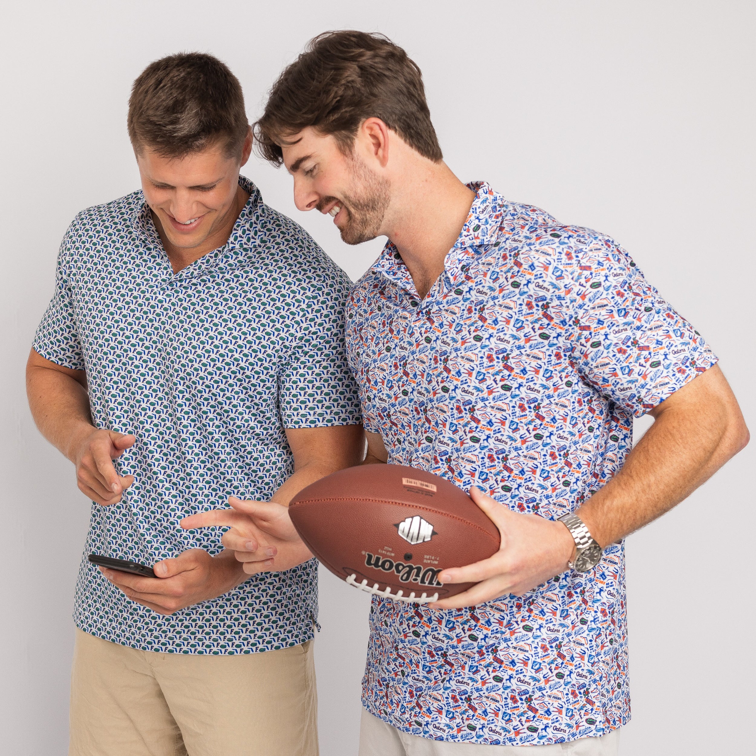 Two men wearing patterned shirts holding a football and a phone on a plain background