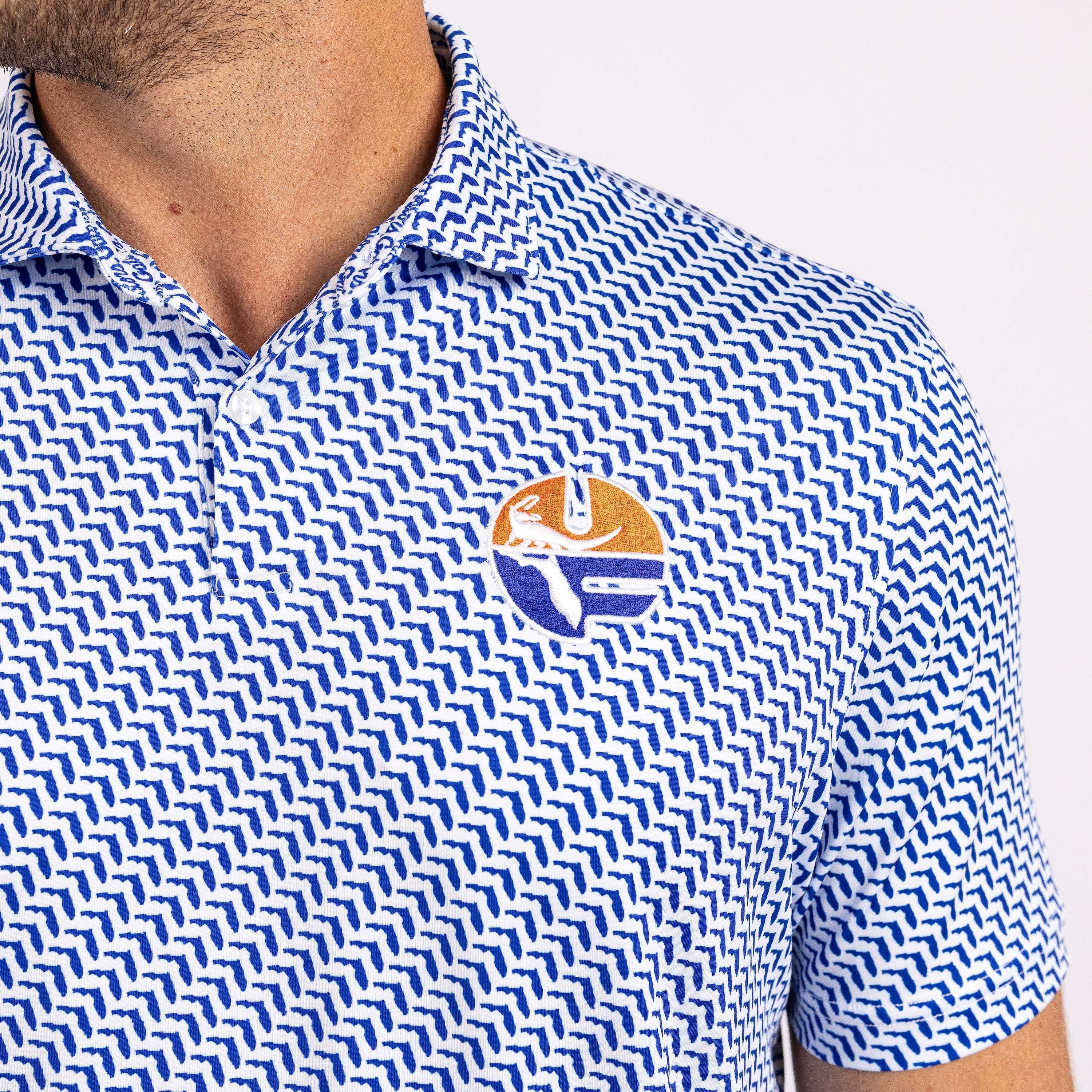 Close-up of a man wearing a blue and white patterned polo shirt with a circular embroidered logo on the chest.