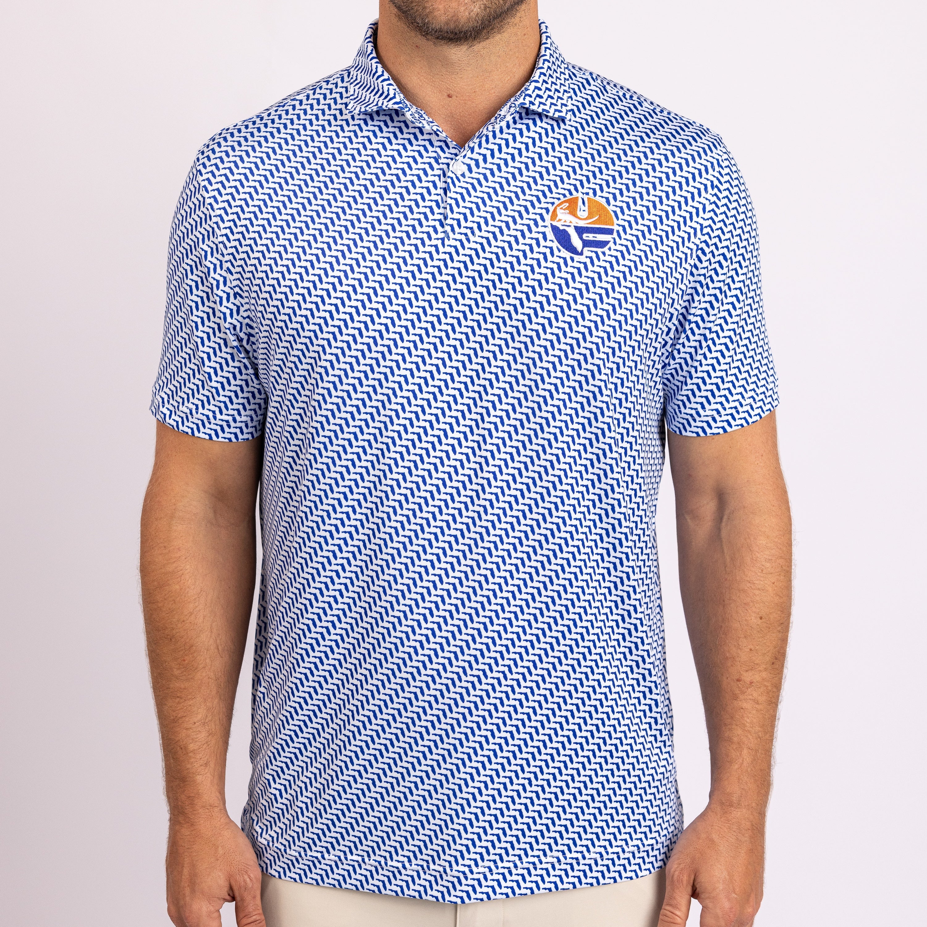 A man wearing a blue and white patterned short-sleeve polo shirt with a small embroidered logo on the left chest, photographed against a light gray studio background.