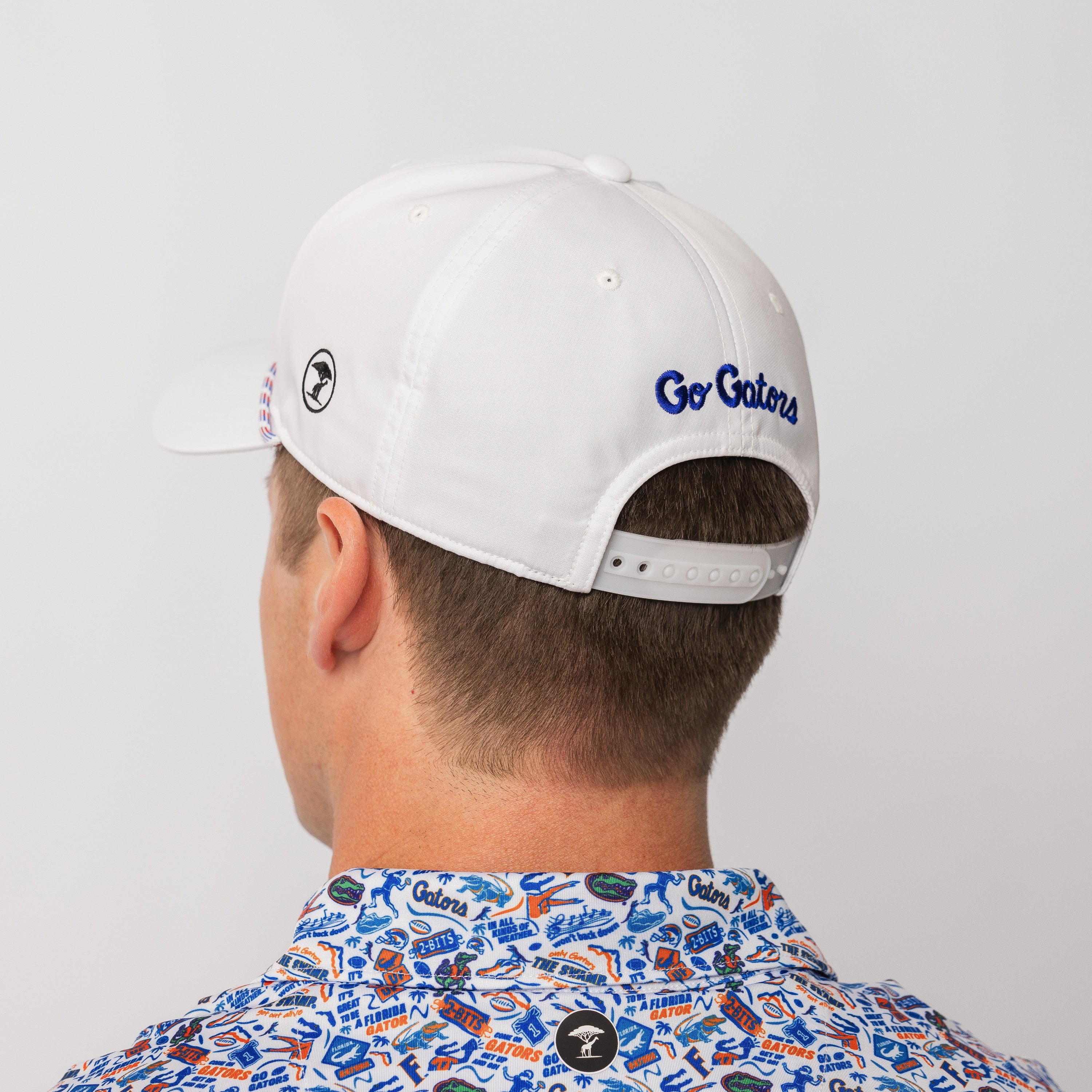 A man shown from the back wearing a white baseball cap with blue 'Go Gators' embroidery on the side and a colorful patterned collared shirt against a light gray background.
