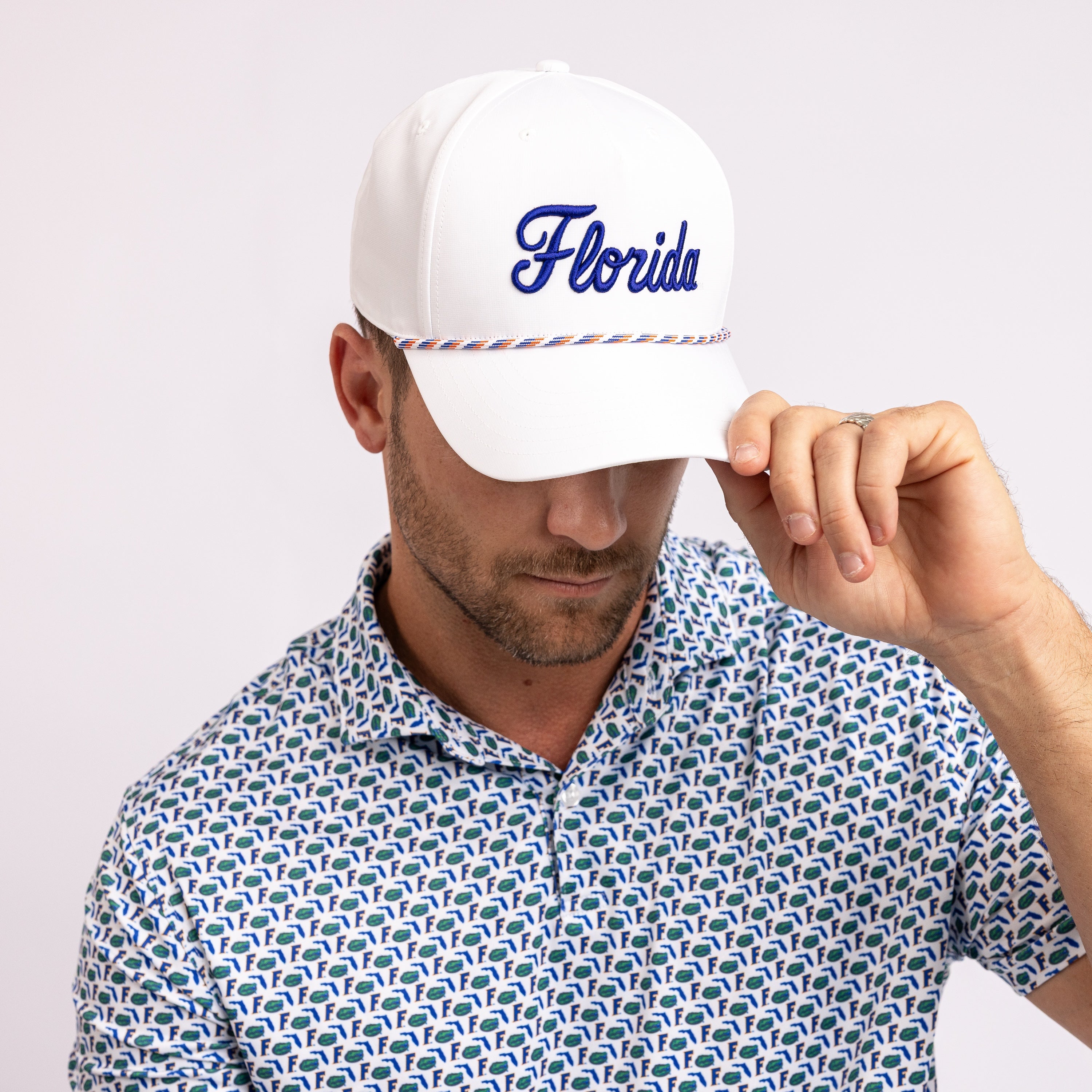 A man wearing a white baseball cap with 'Florida' embroidered in blue script on the front, paired with a blue and white patterned polo shirt, against a light gray studio background.