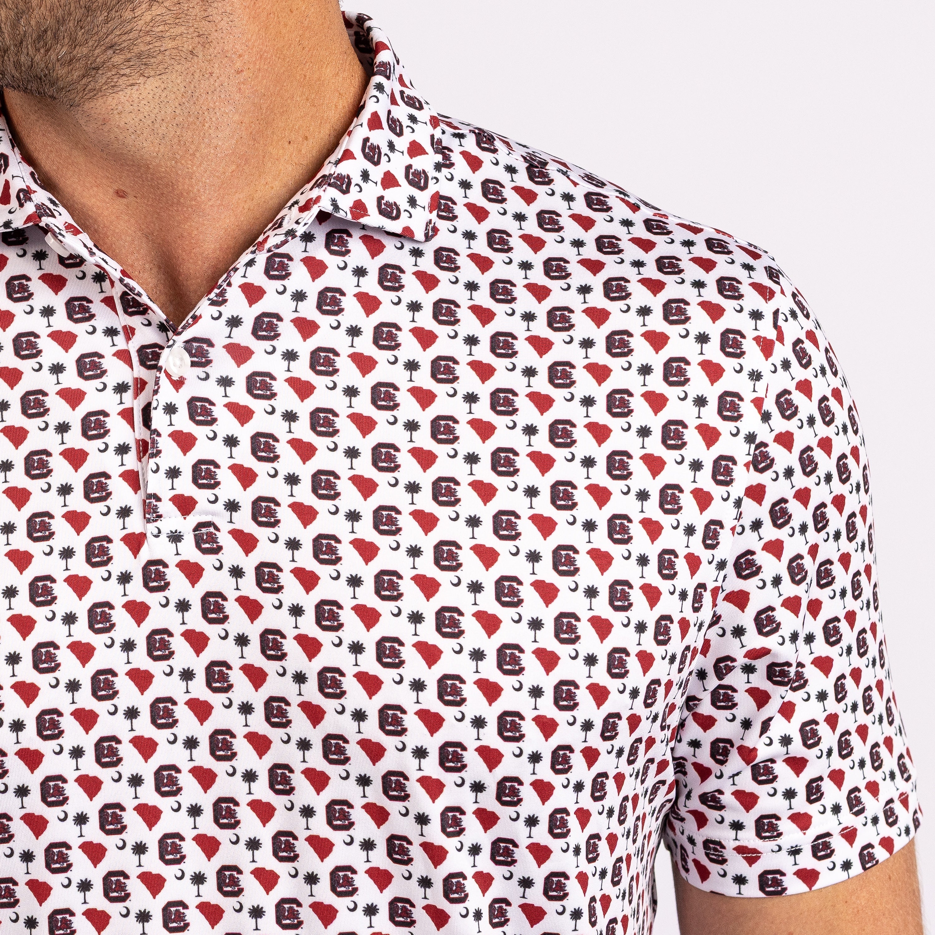 A close-up of a man wearing a white short-sleeve polo shirt with an all-over repeating pattern dark brown 'C' logos and small black palm trees.