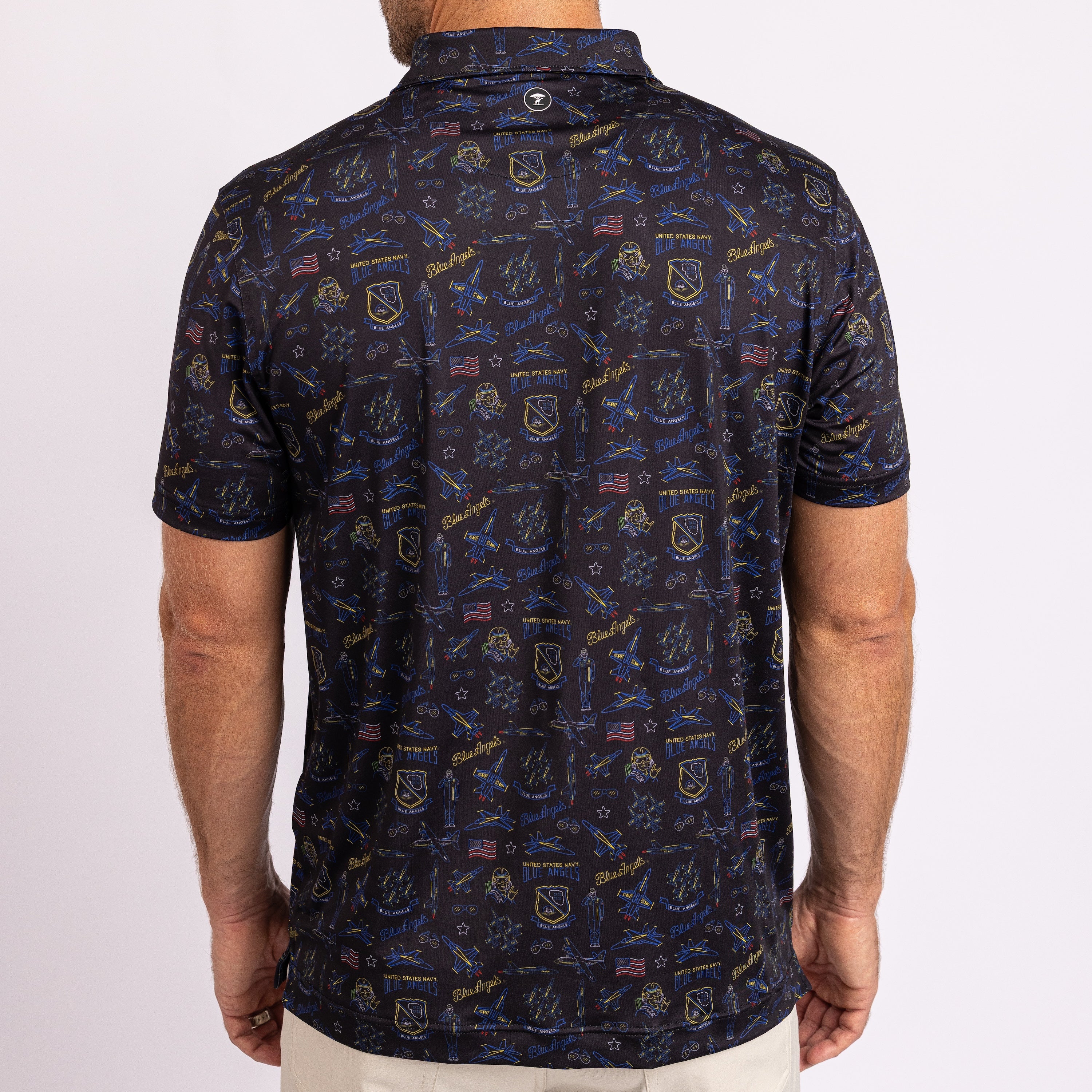 A man wearing a short-sleeve polo shirt from the back, featuring a dark navy blue background covered in a detailed pattern of military insignia, flags, and text in blue, gold, and white.