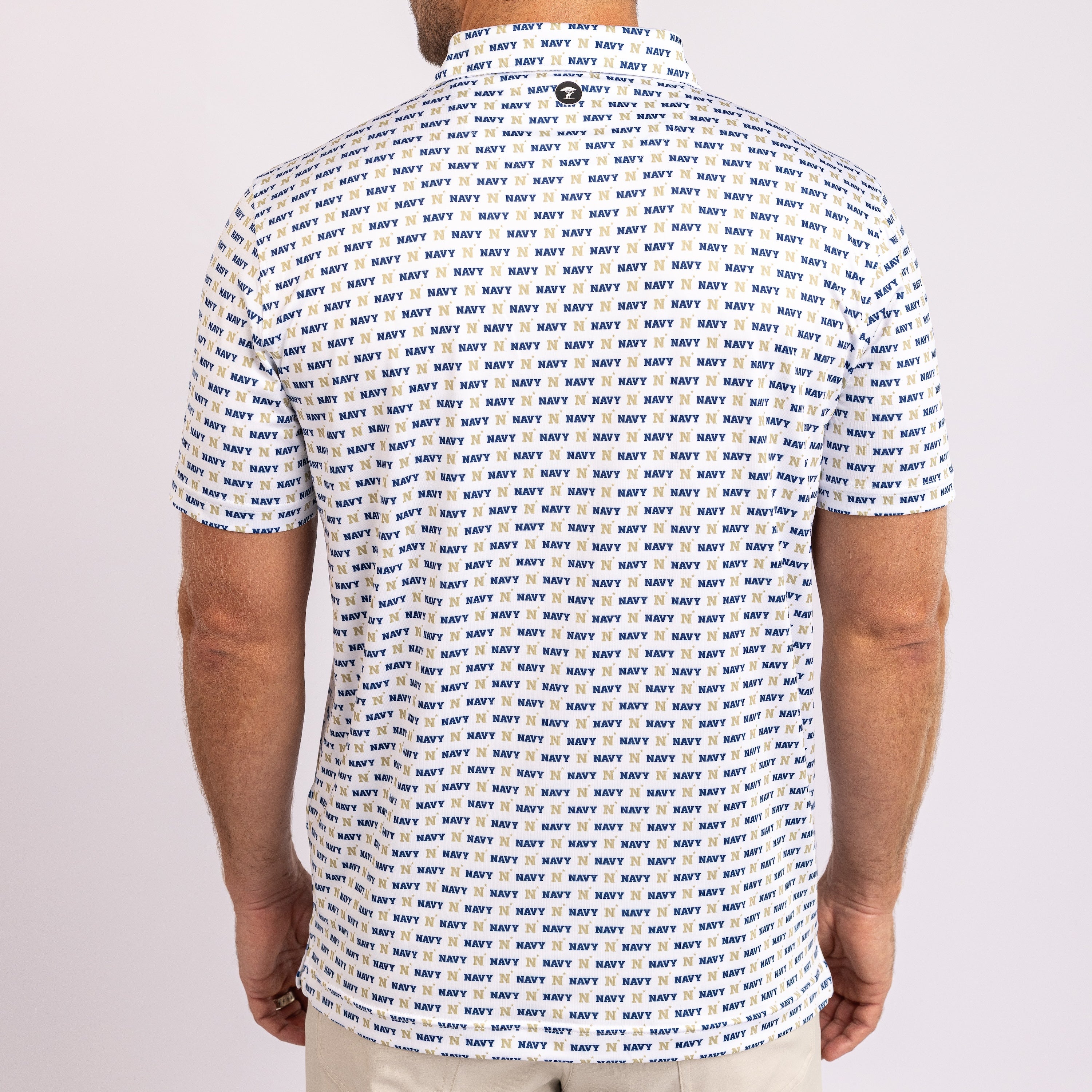 A man viewed from the back wearing a short-sleeve collared shirt covered in an all-over navy blue 'NAVY' text print on a white base, paired with light beige pants against a plain light gray studio background.