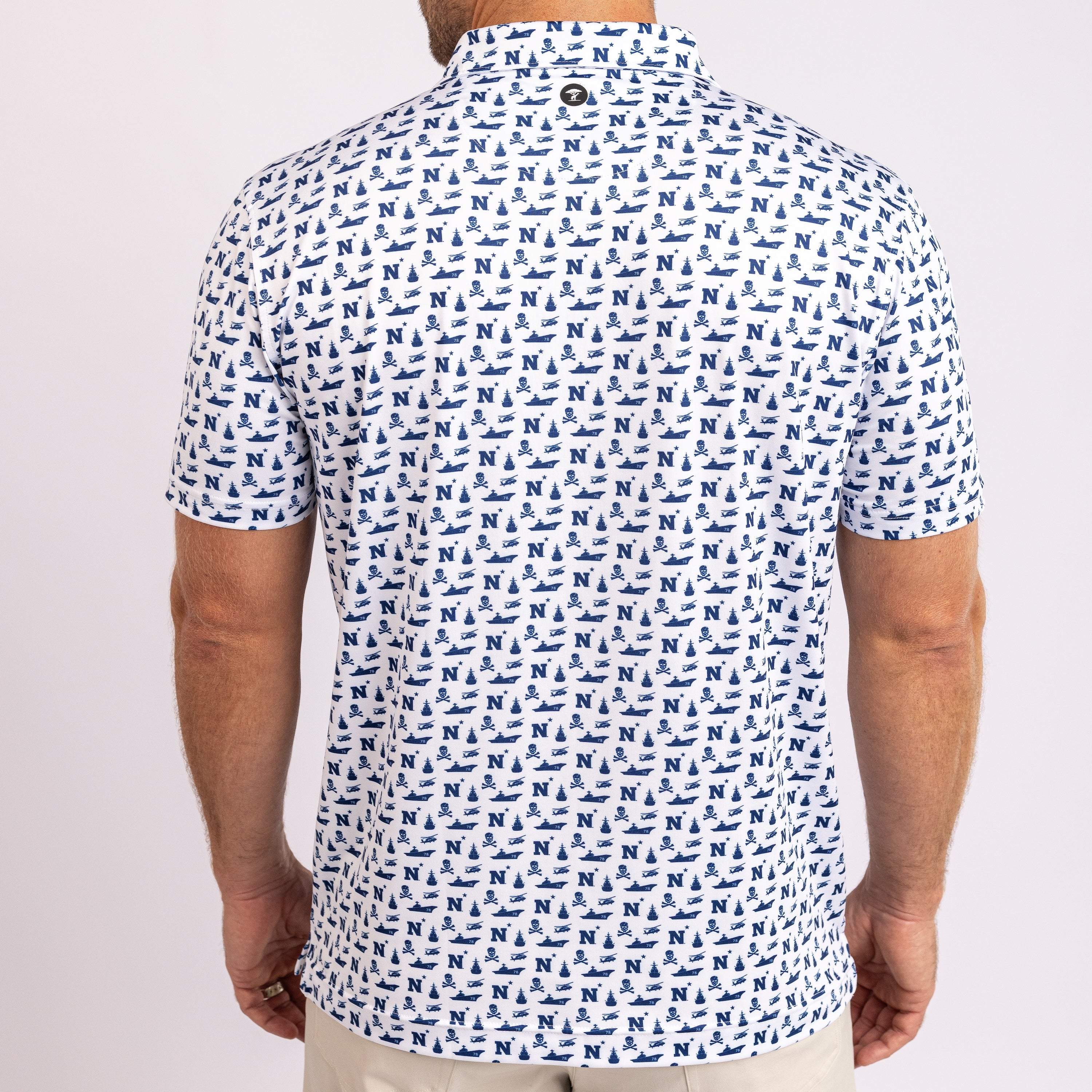 A man viewed from the back wearing a short-sleeve polo shirt with an all-over repeating blue monogram pattern on a white base, paired with light beige pants against a plain light background.