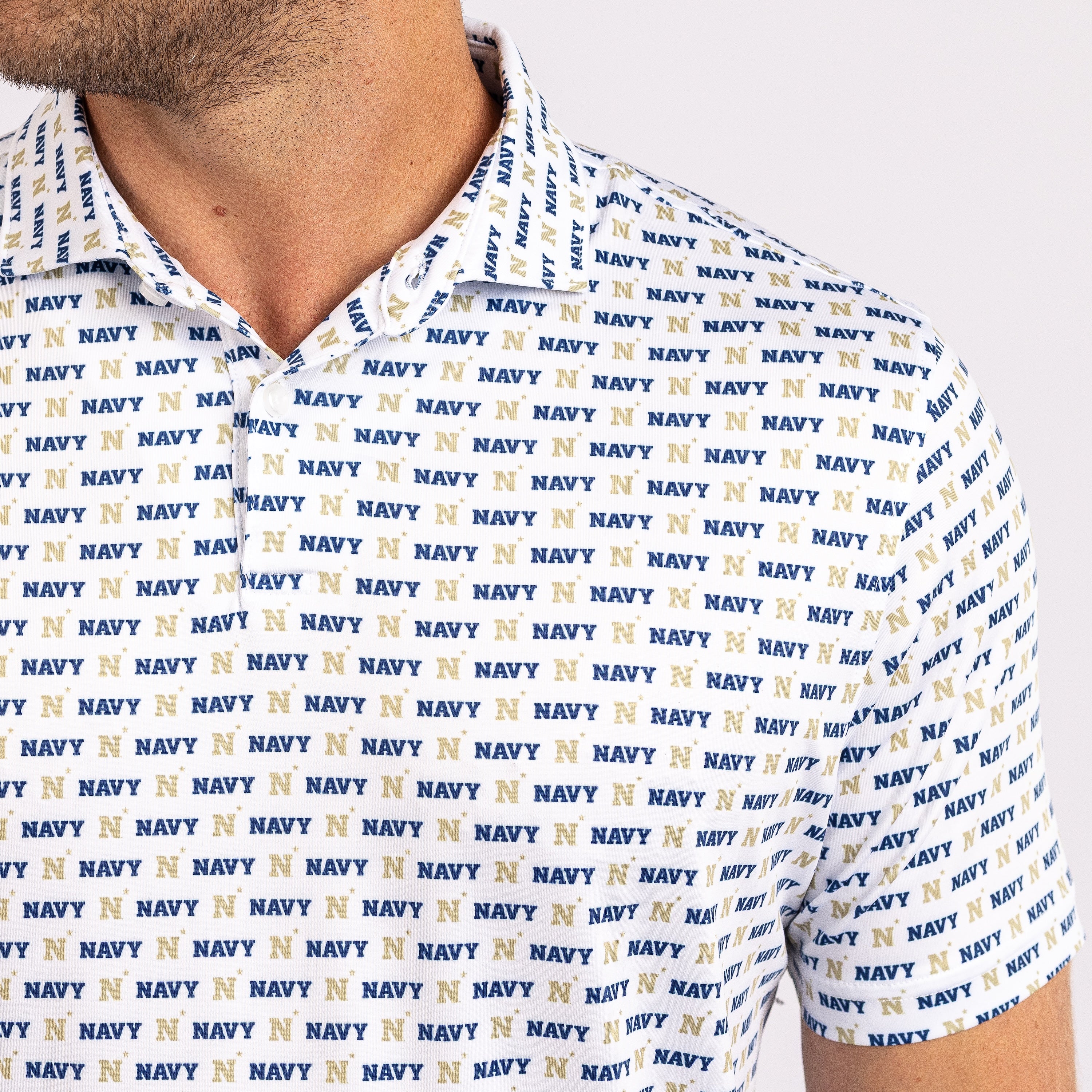 Close-up of a white short-sleeve polo shirt with an all-over navy and gold 'NAVY N' repeating pattern, worn by a model.